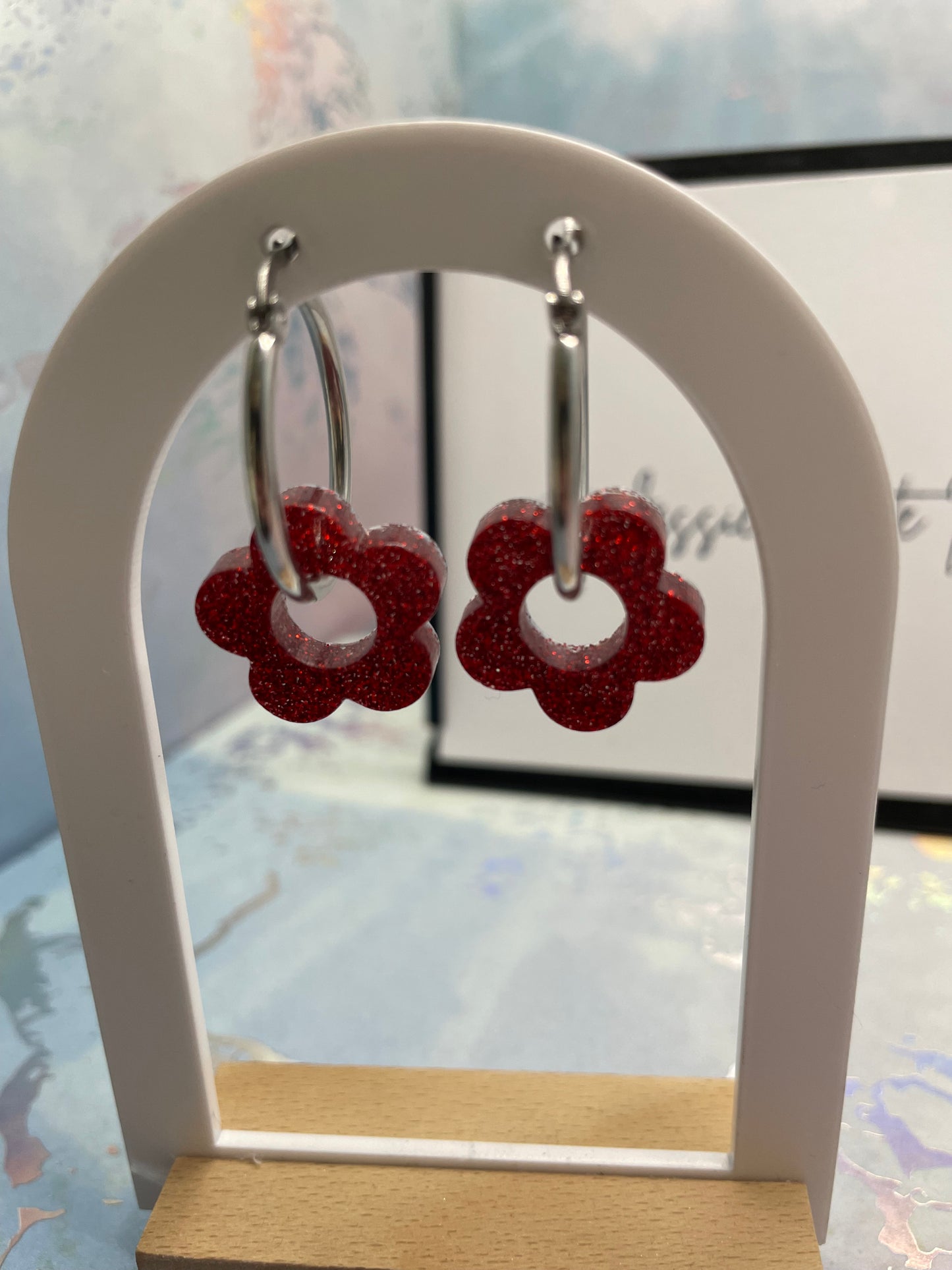 Red flower-shaped earrings on a white stand with a blurred background
