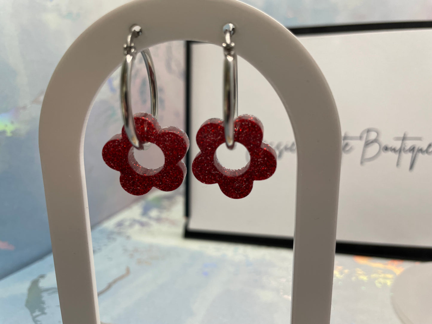 Red flower-shaped earrings on a white stand with a blurred background