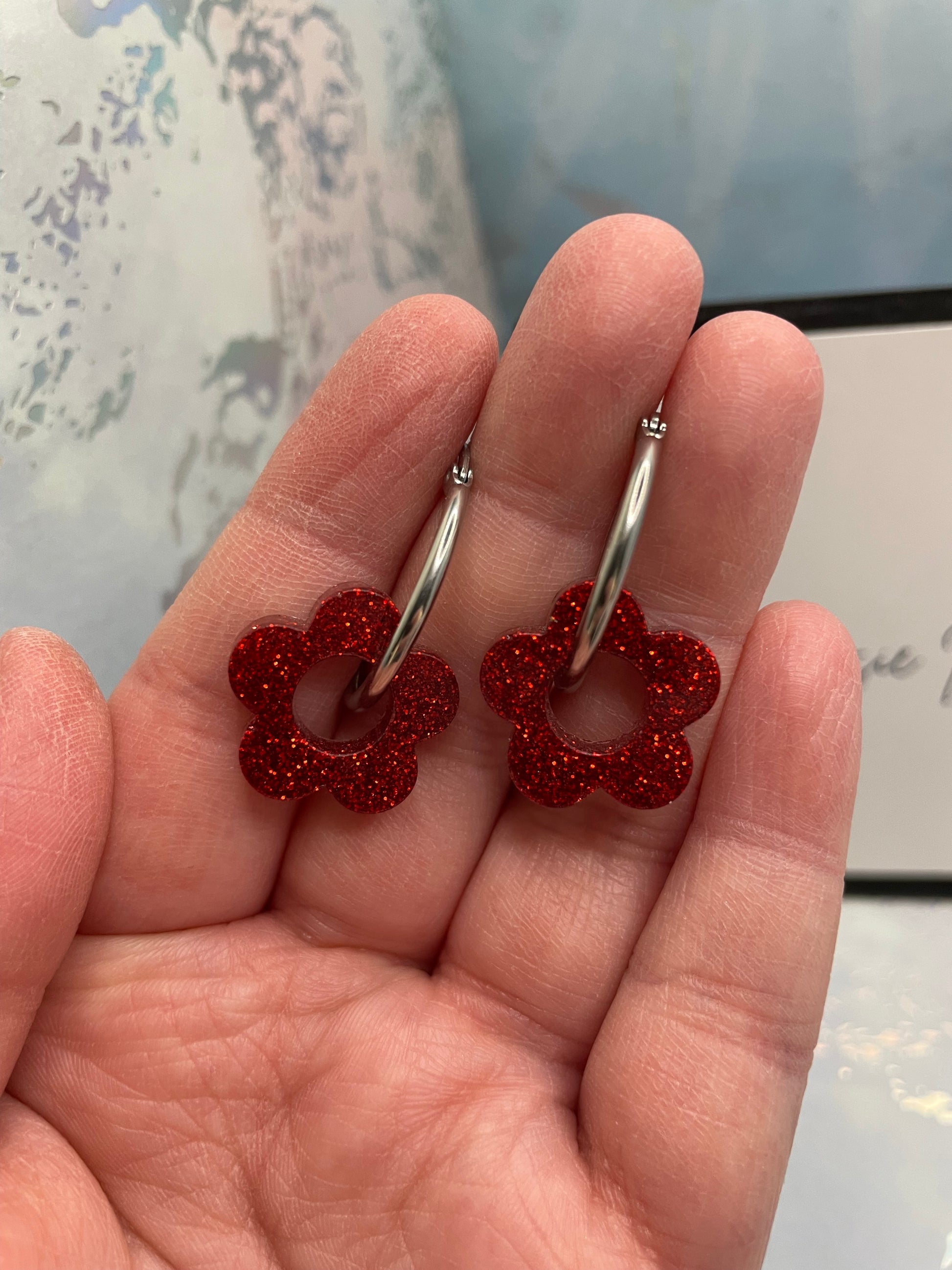Red flower-shaped earrings held in a hand with a blurred background