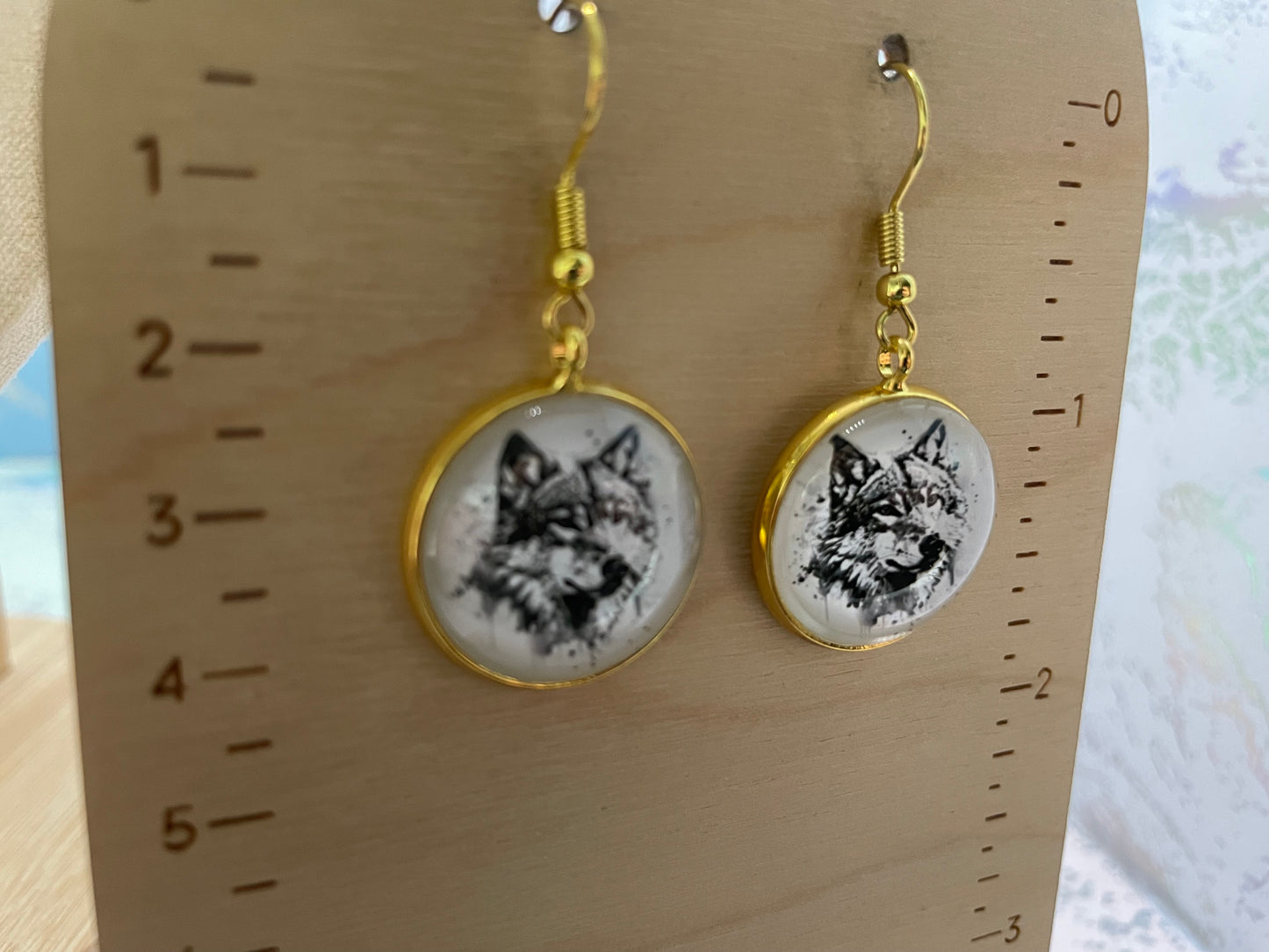 Pair of earrings with wolf design on a wooden ruler