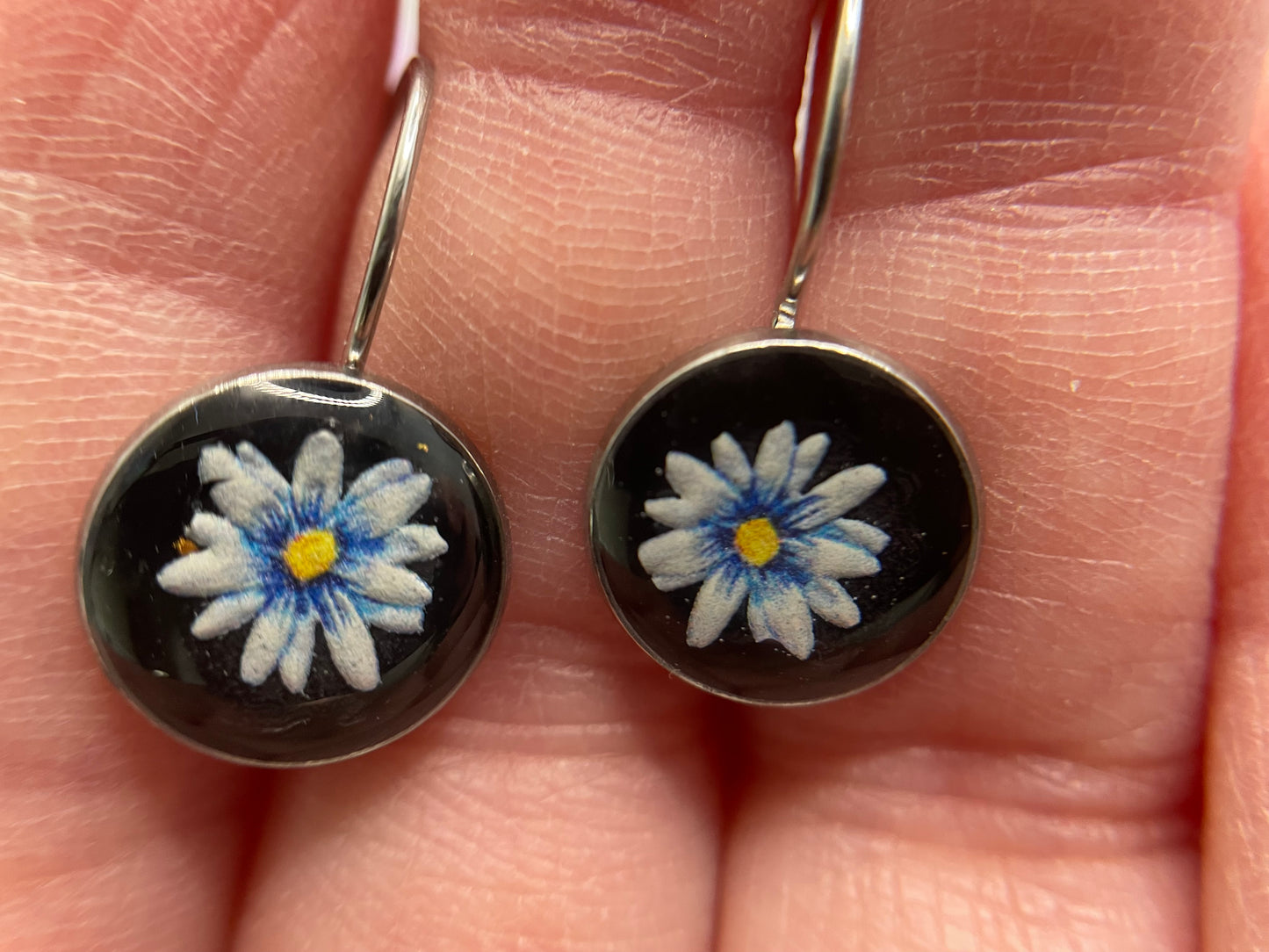 Mini Floral on Black earrings held between fingers on a light skin background