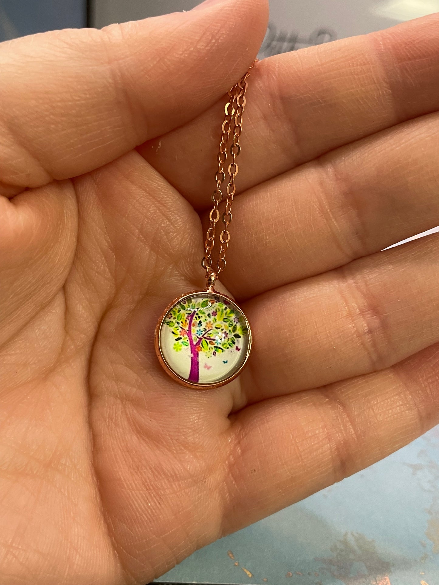 Necklace with a round pendant featuring a colorful design held in a hand.