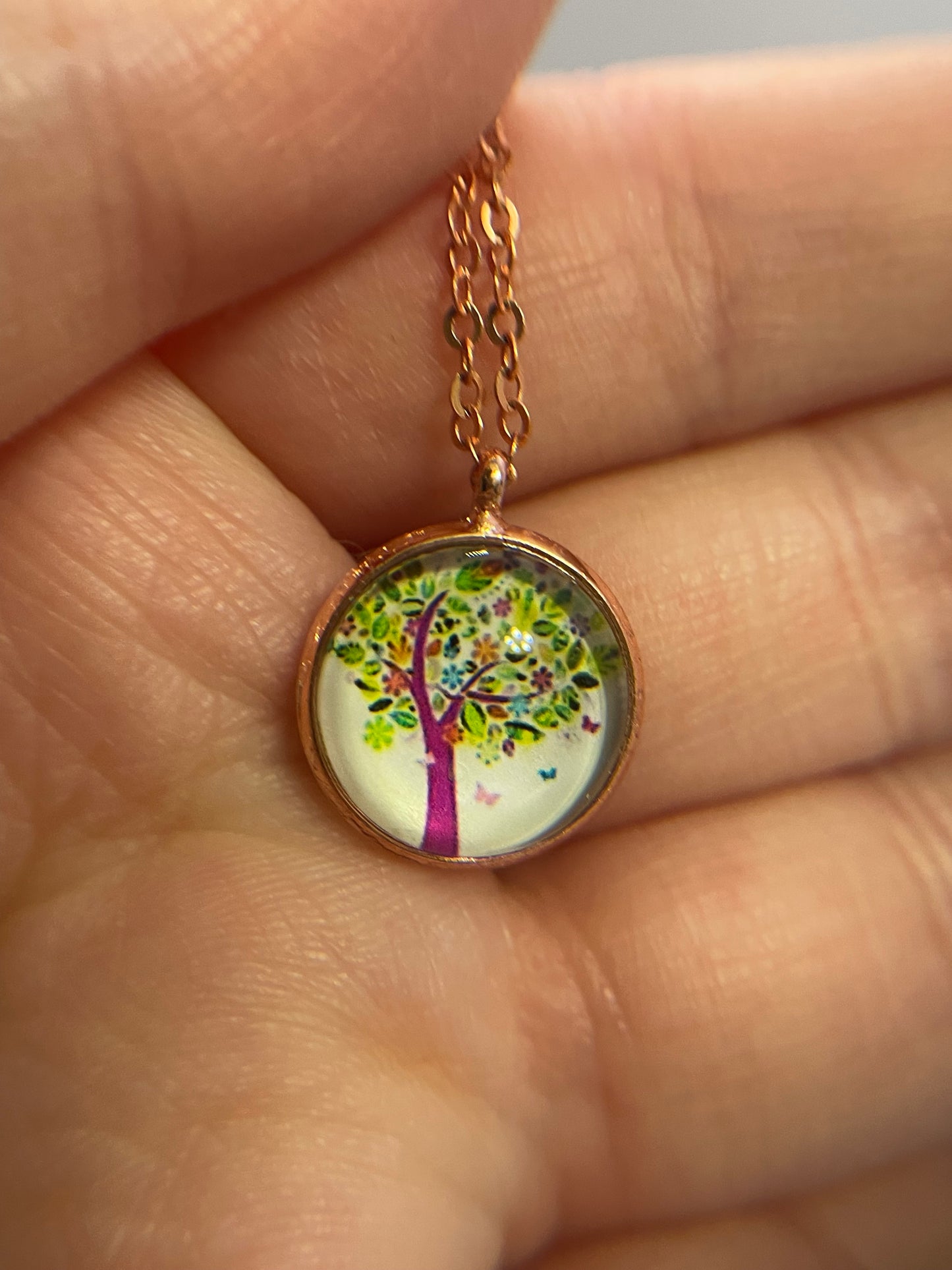 Necklace with a round pendant featuring a colorful design held between fingers.