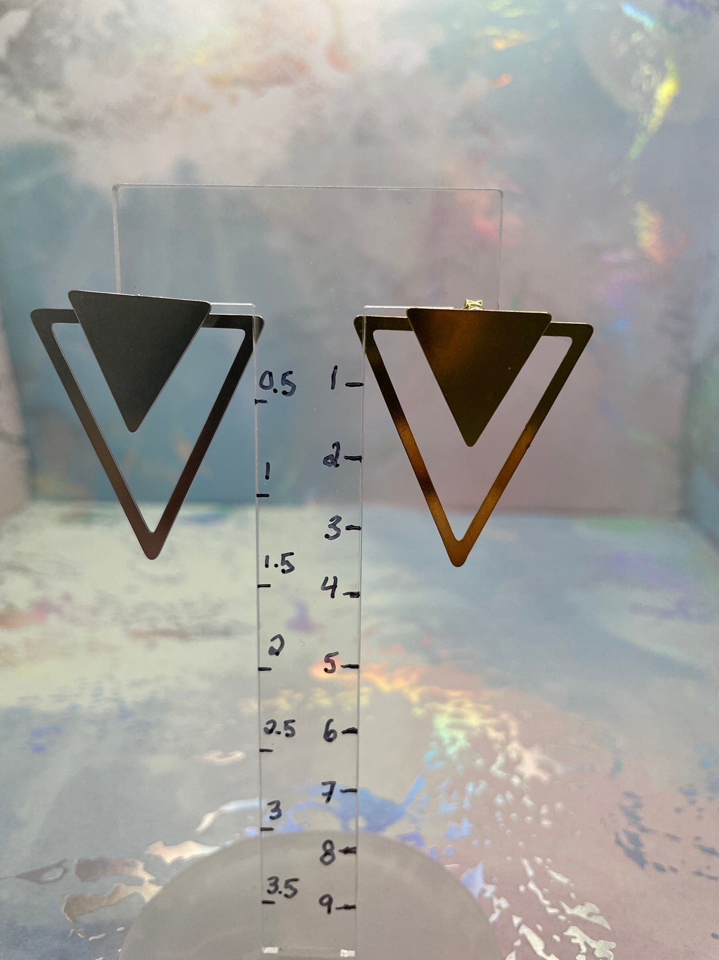 Metal ruler with Convertible Triangle Earrings on a reflective surface