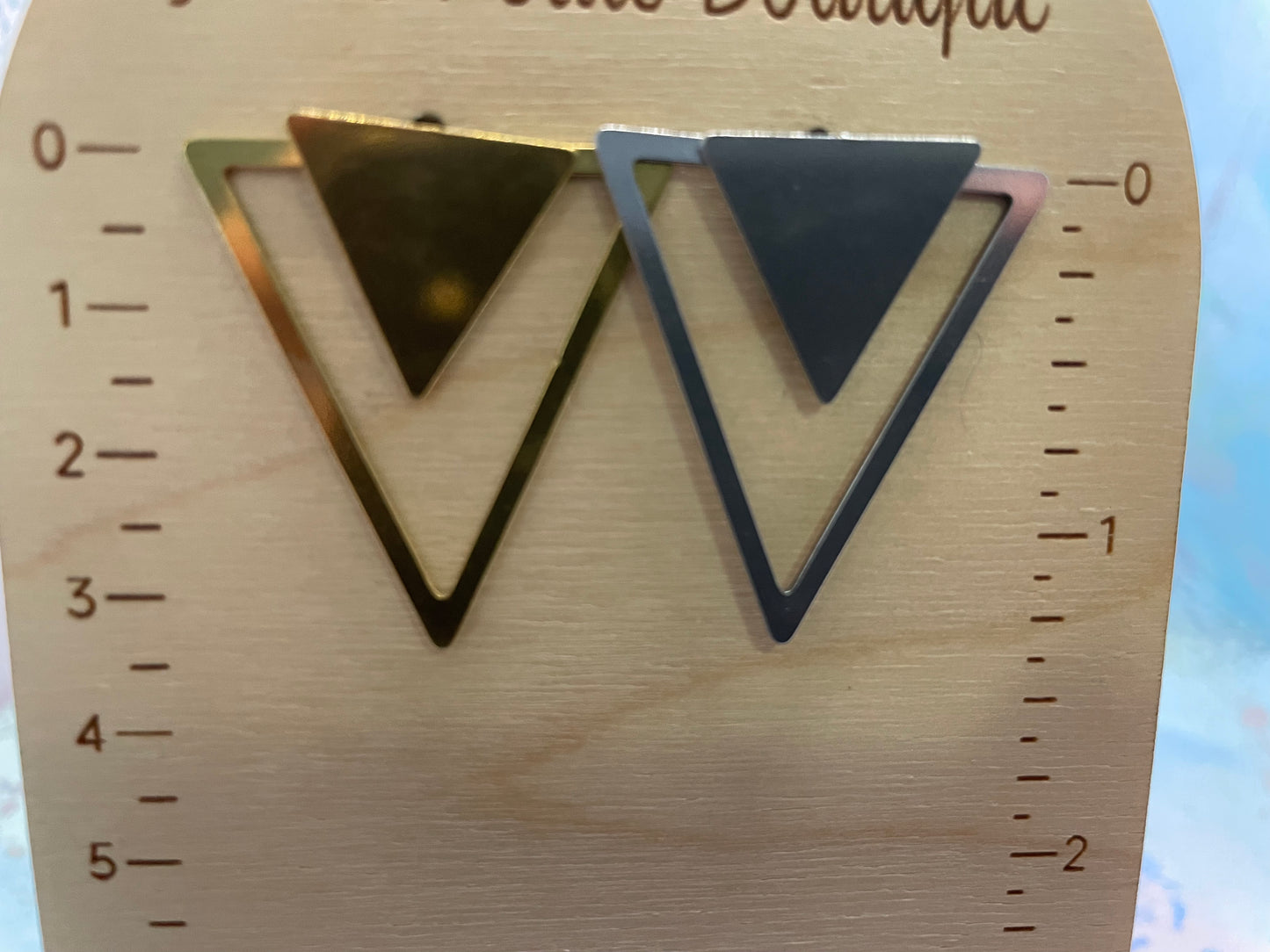 Gold and silver triangle earrings on a wooden ruler
