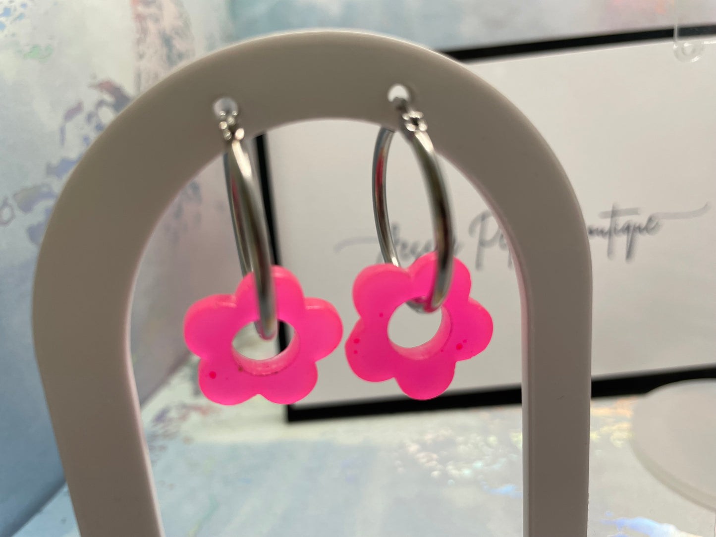 Pink flower-shaped earrings on a white stand with a blurred background