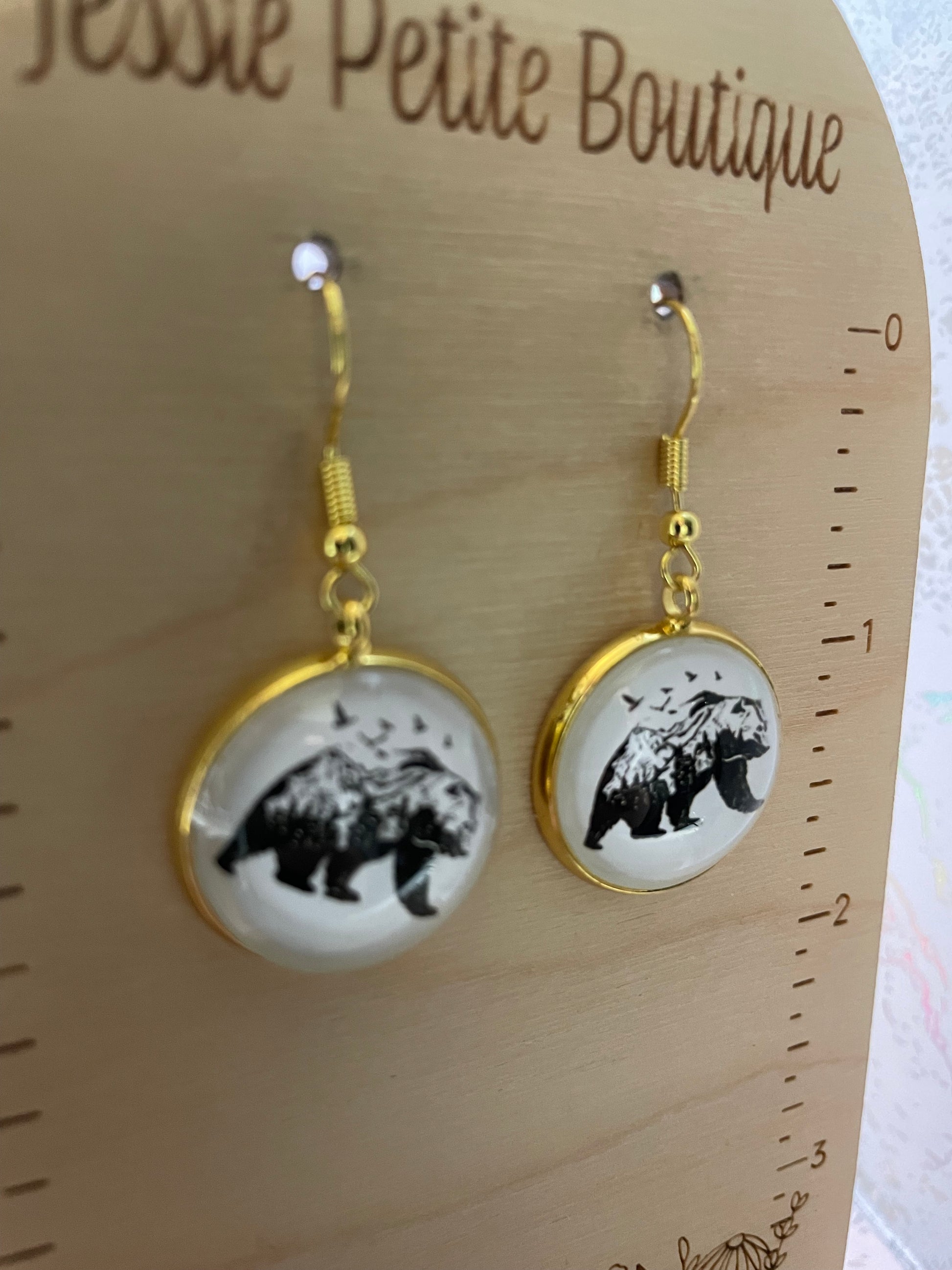 Pair of earrings with black and white designs on a wooden surface with 'Jessie Petite Boutique' branding.
