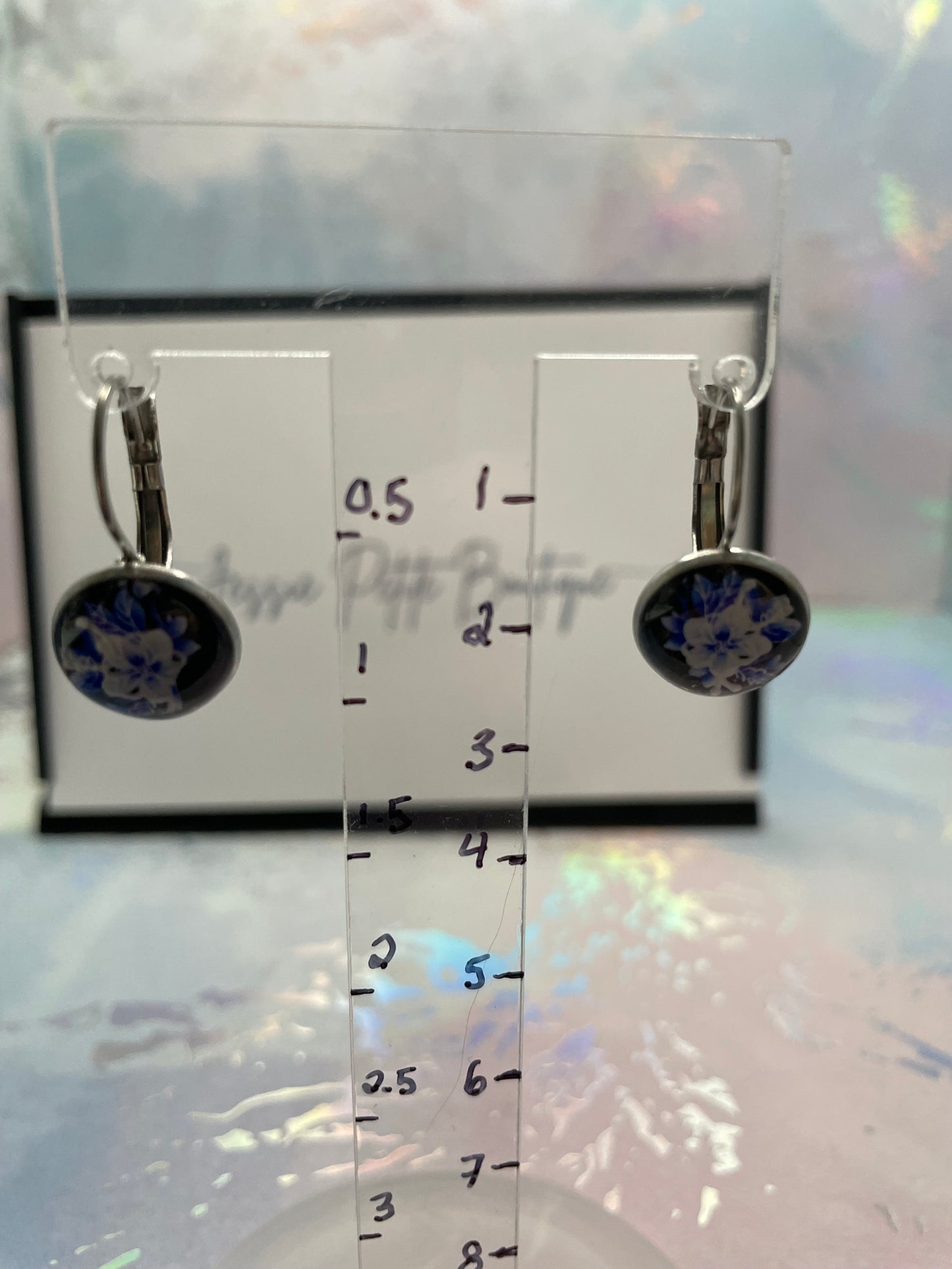 Jewelry display card with two earrings on a reflective surface