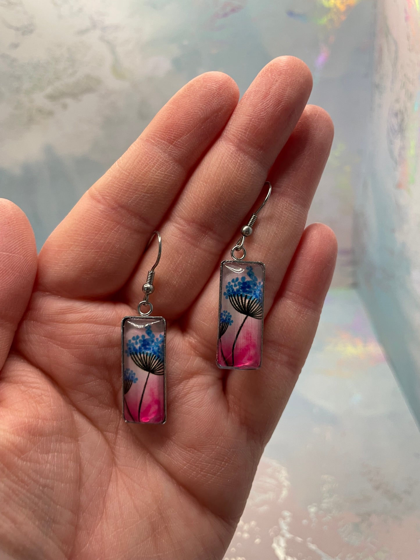 Hand holding a pair of floral earrings with a light background