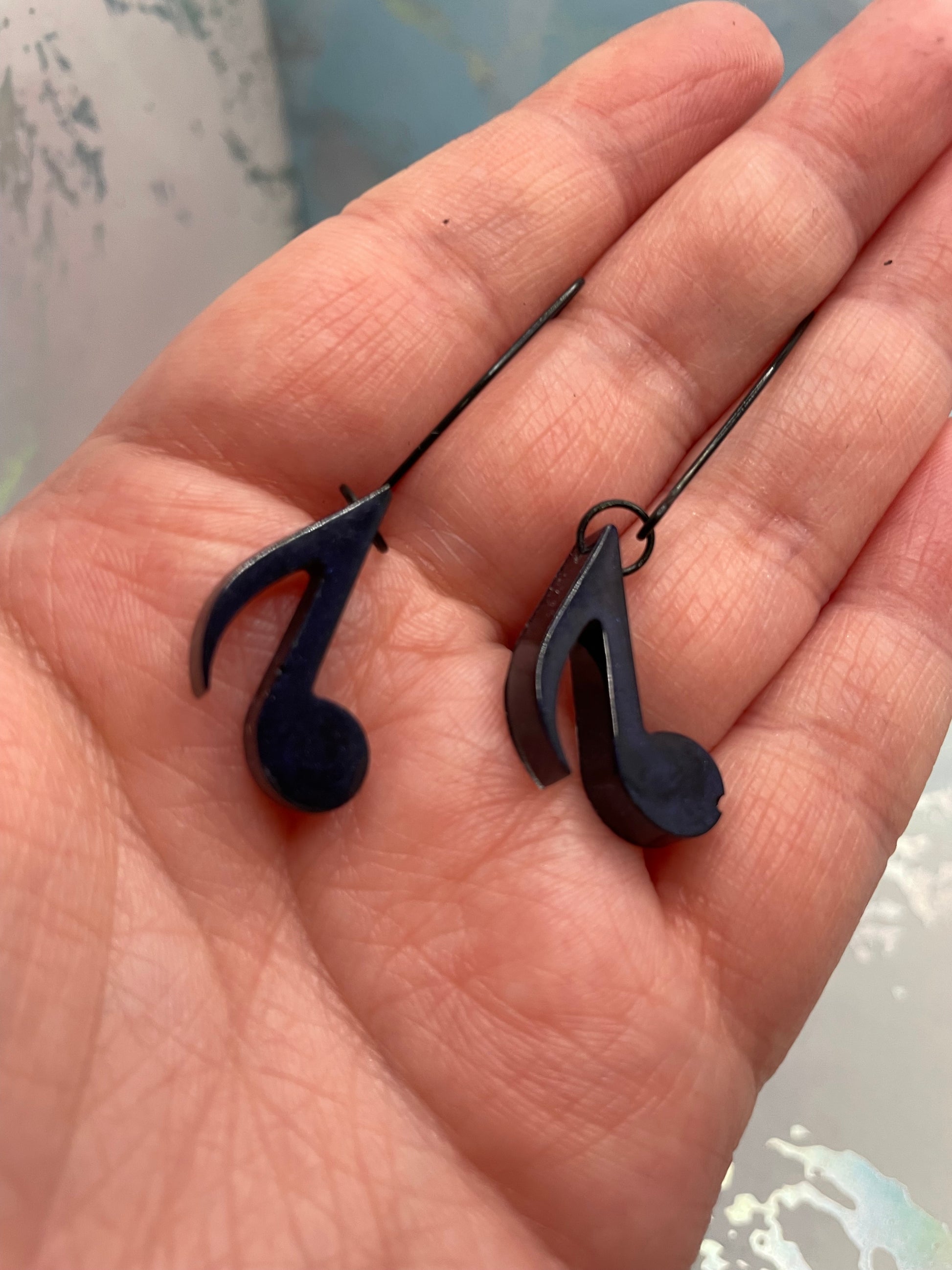 Dark Blue Music Note Earrings held in a hand with a blurred background