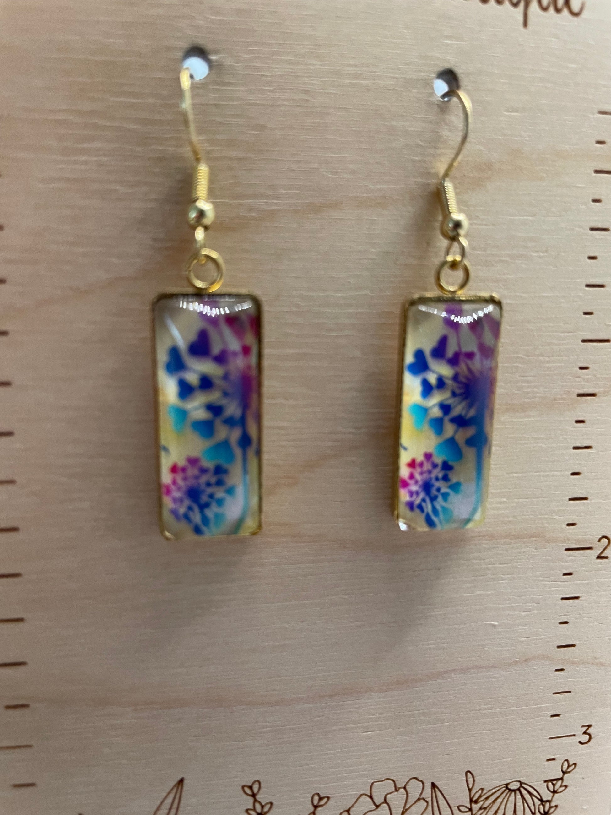 Pair of floral-patterned earrings on a wooden surface with a ruler for scale.