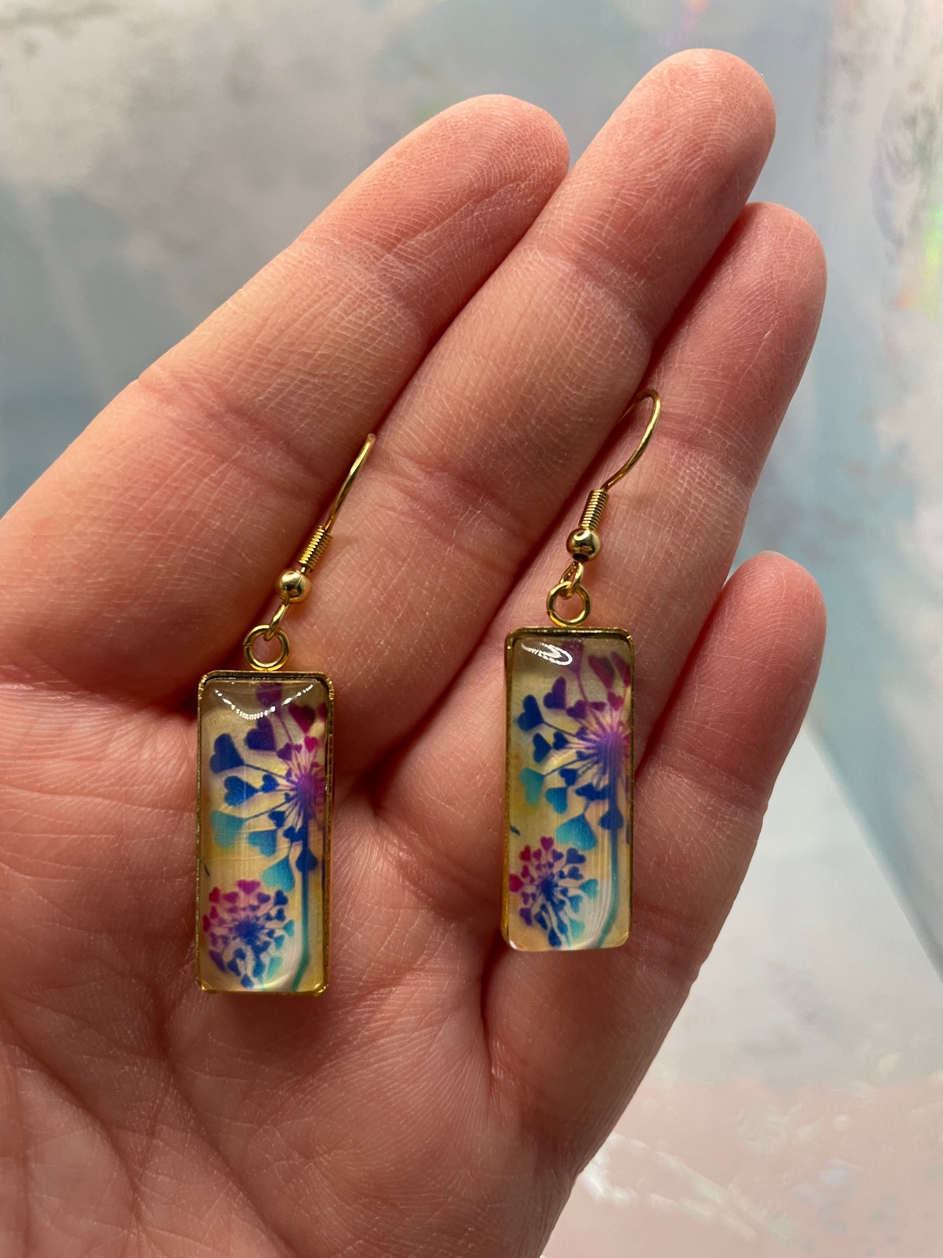 Floral earrings held in a hand with a blurred background