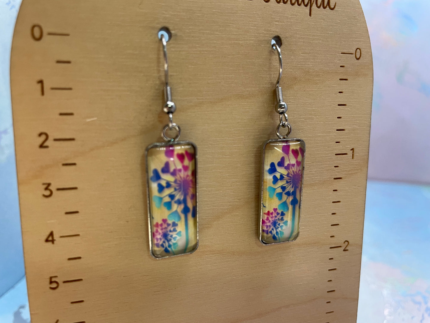 Pair of floral rectangular earrings on a wooden display card with measurement scale.