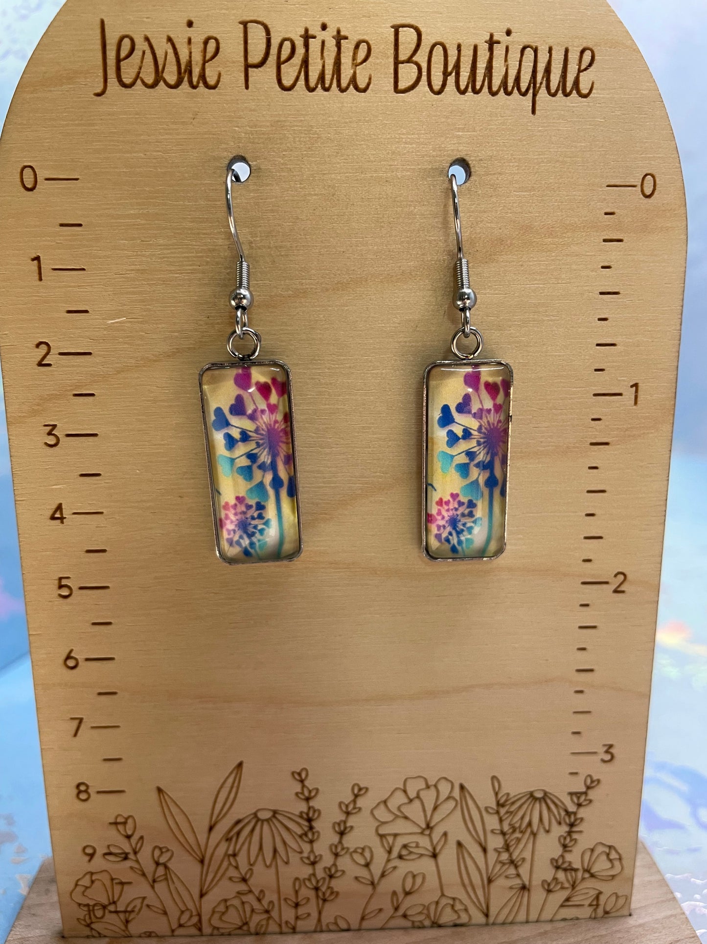 Colorful rectangular earrings on a wooden ruler with 'Jessie Petite Boutique' branding.
