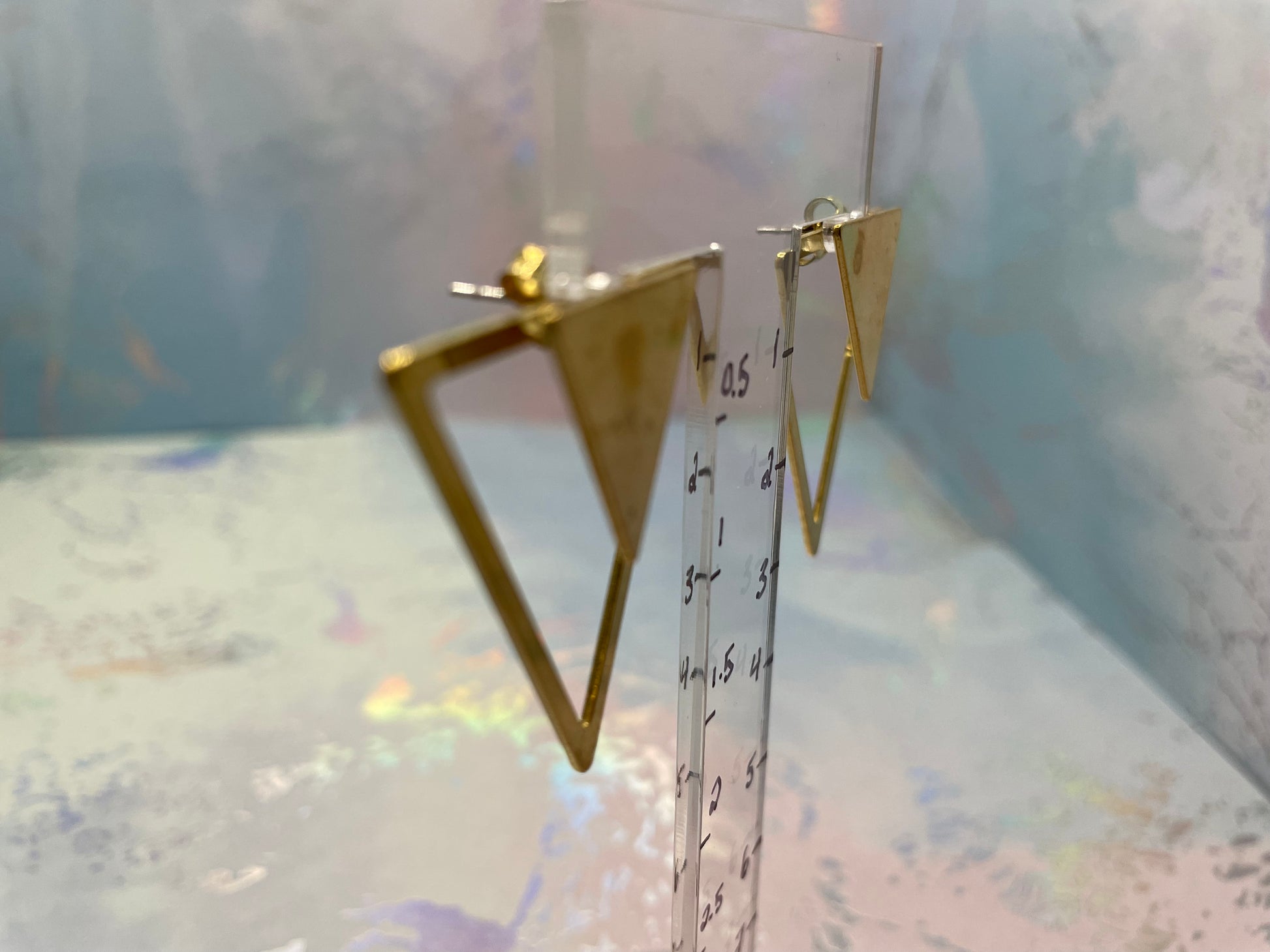 Gold triangle-shaped earrings on a clear stand with a blurred background