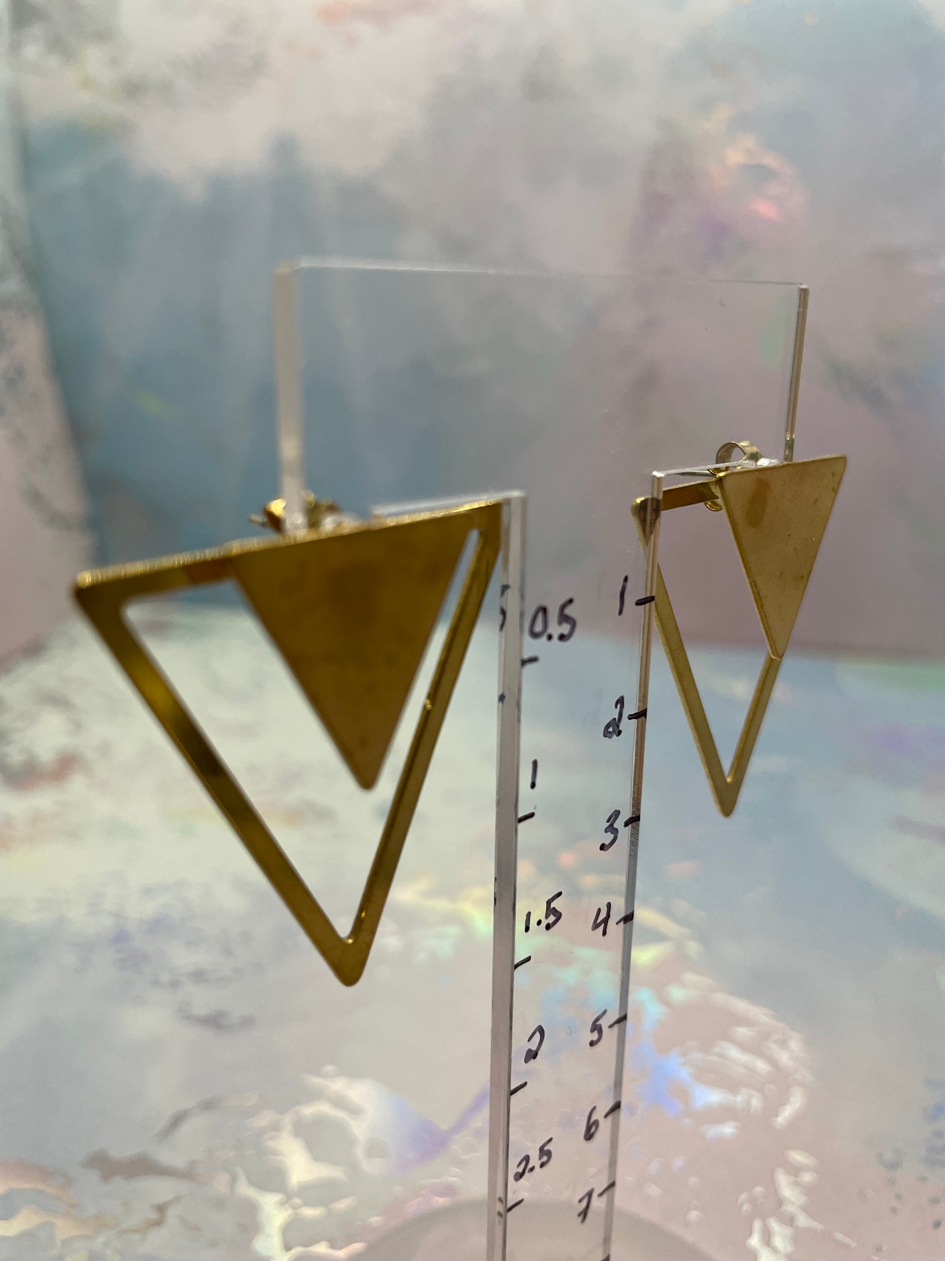 Gold triangle earrings with a ruler for scale on a light background