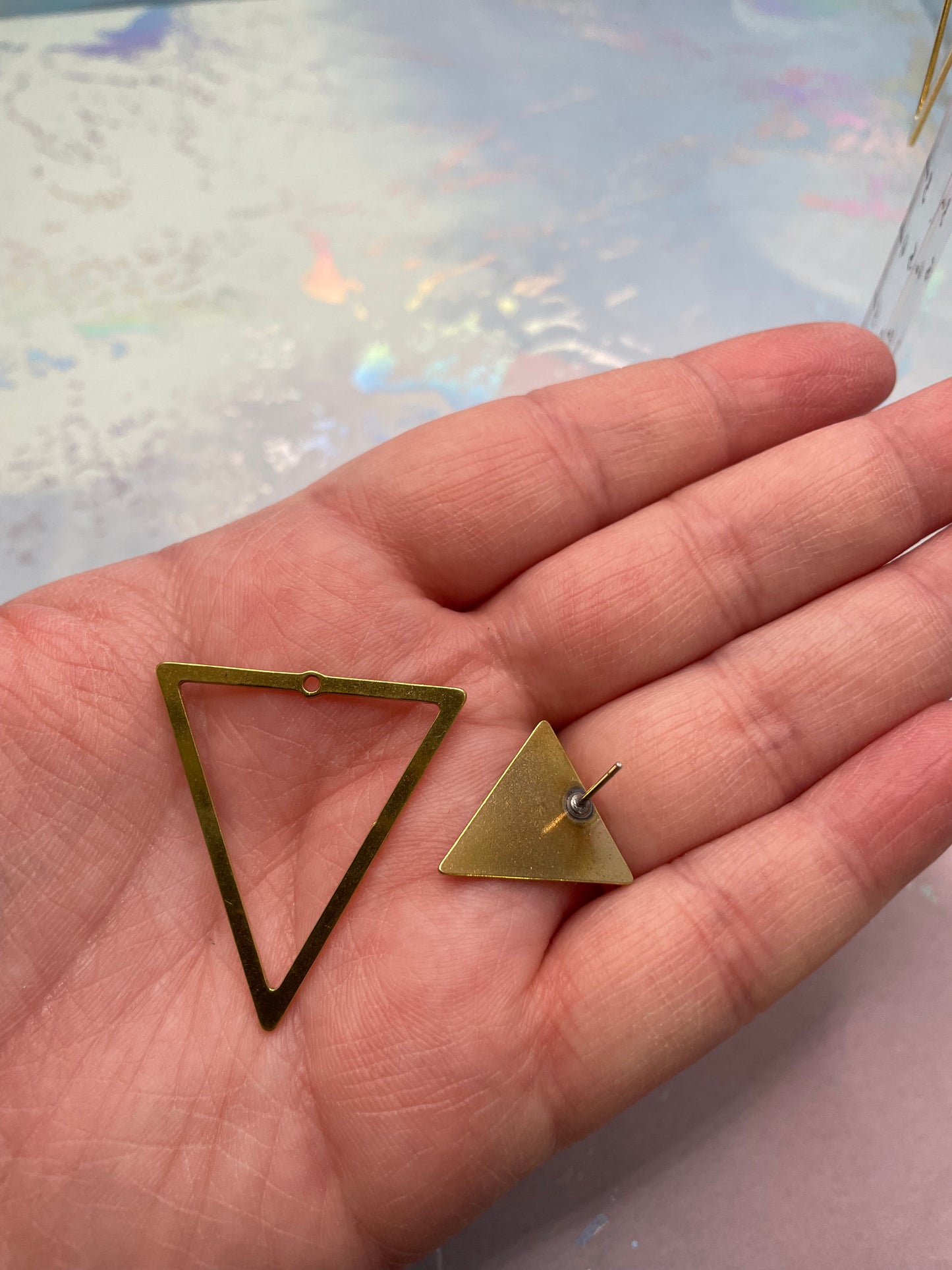Gold triangle-shaped earrings held in a hand with a light background
