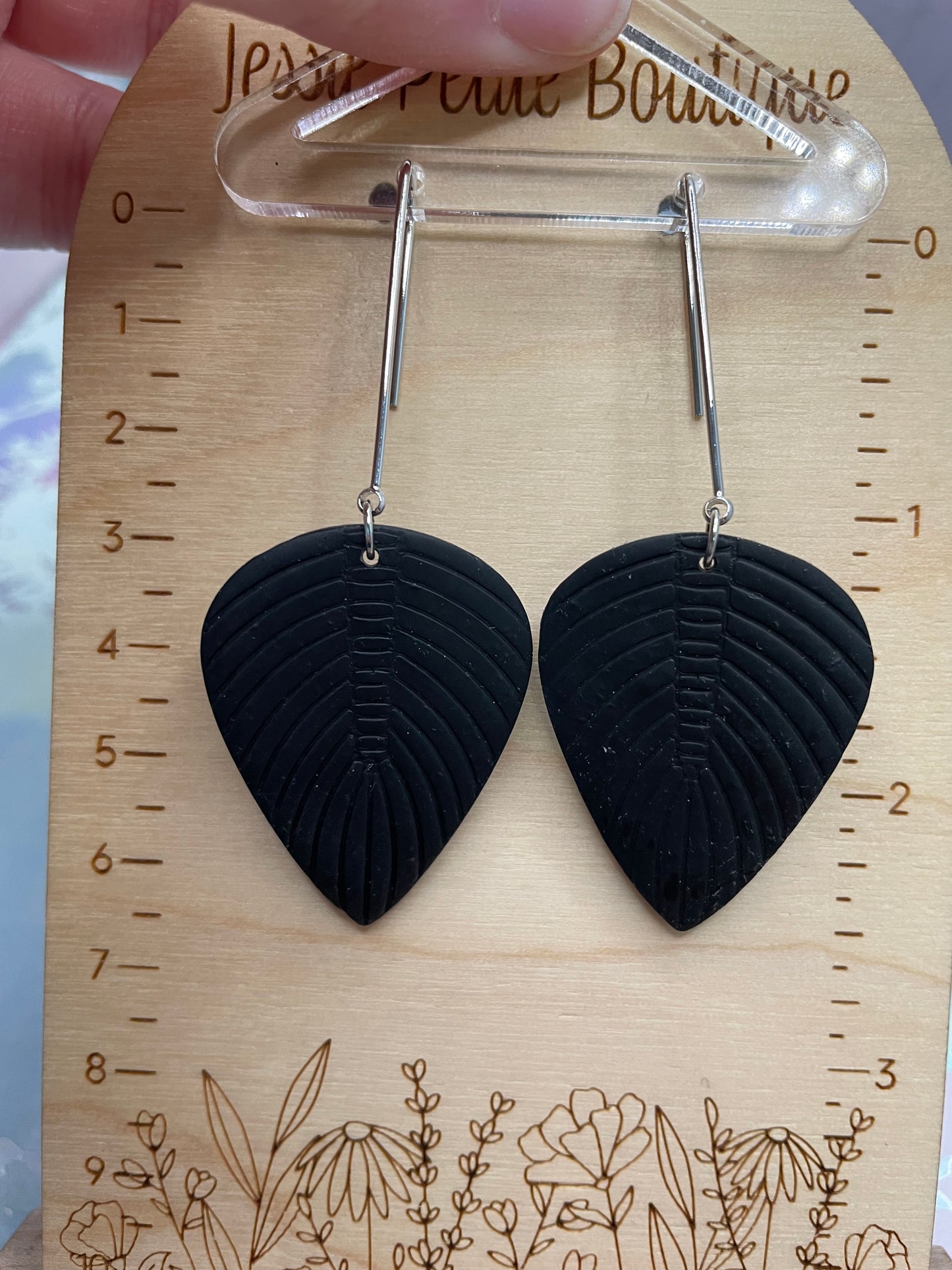 Black leaf-shaped earrings on a wooden display card with measurements.