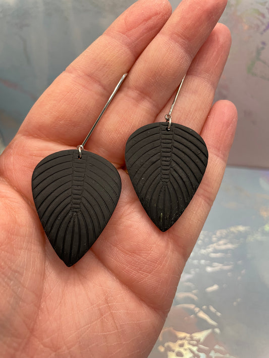 Black leaf-shaped earrings held in a hand with a blurred background