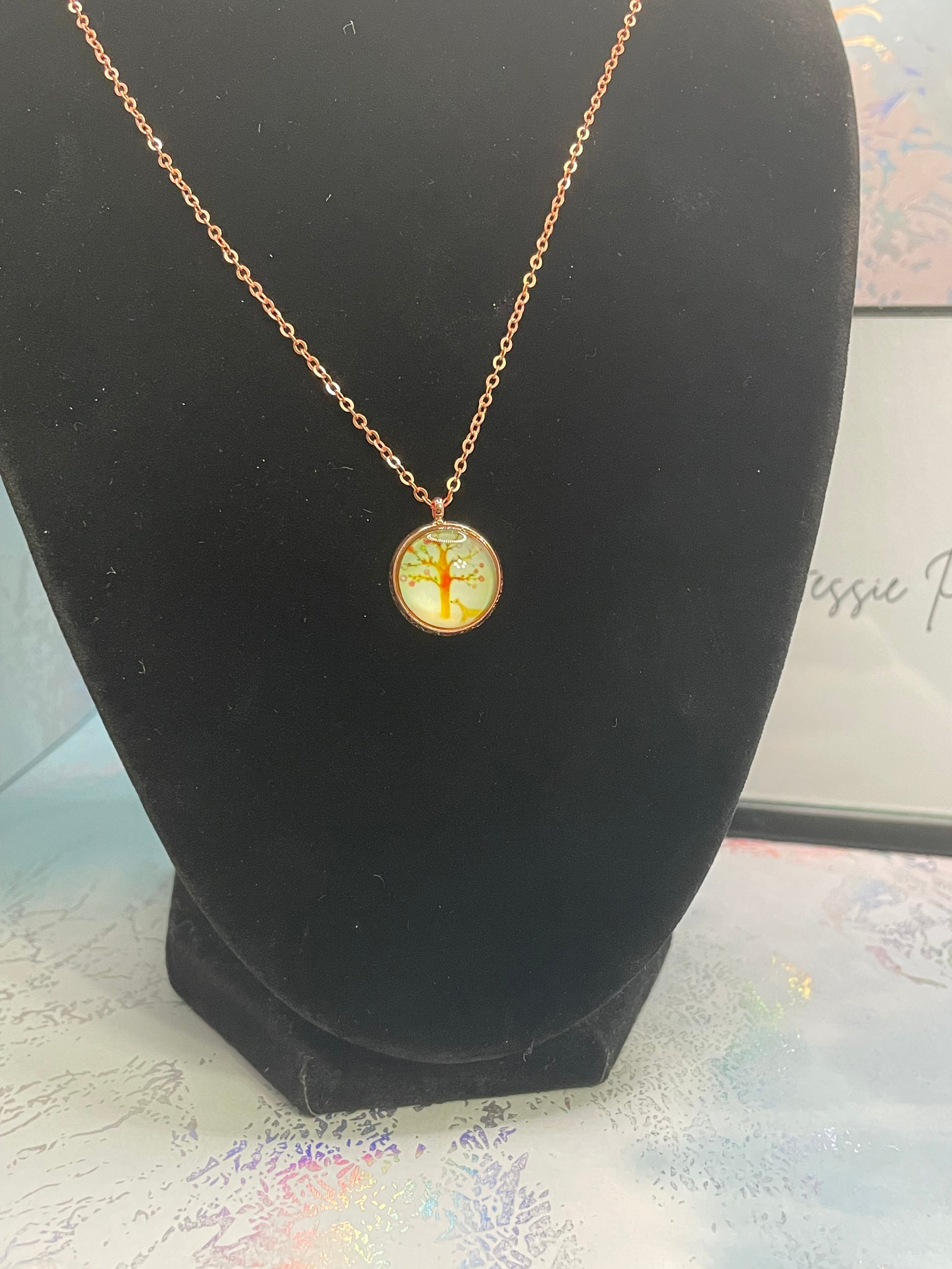 Gold necklace with a round pendant on a black stand.