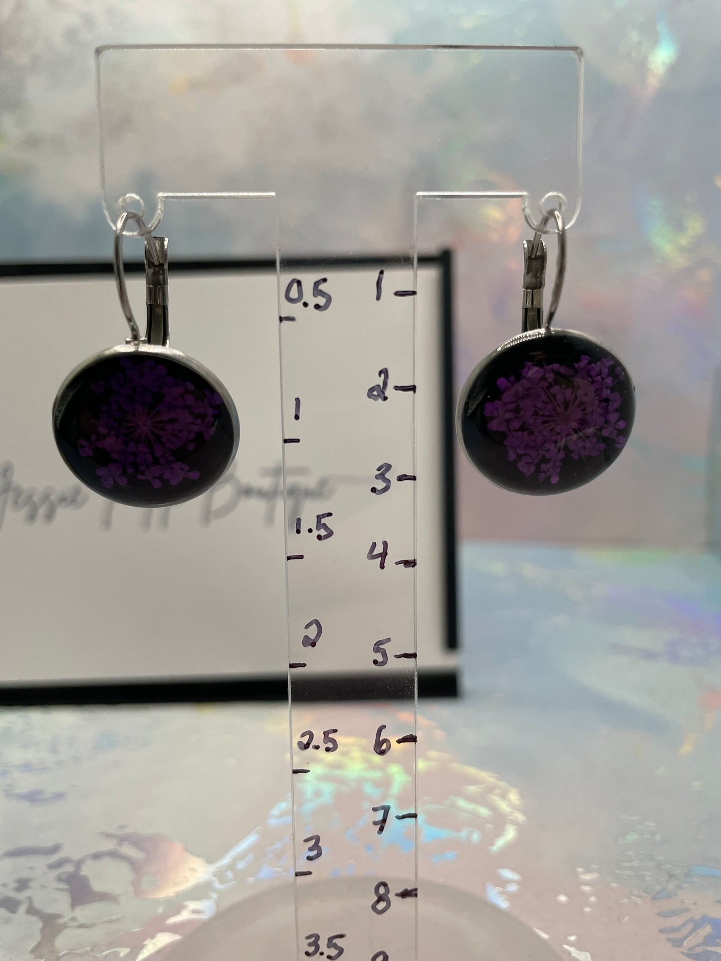 Two purple circular earrings on a clear stand with measurement scale