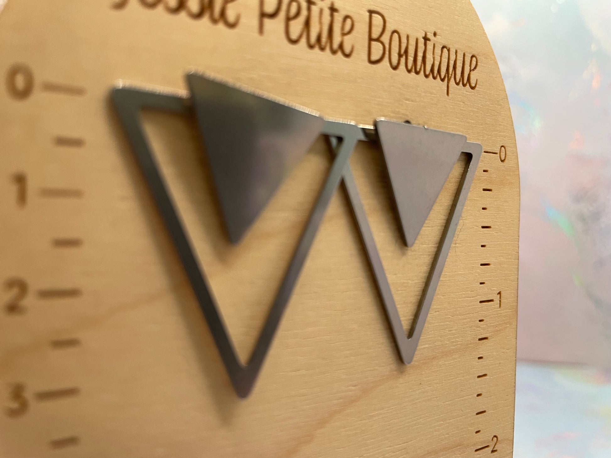 Metal triangle earrings on a wooden scale with 'Petite Petite Boutique' branding.