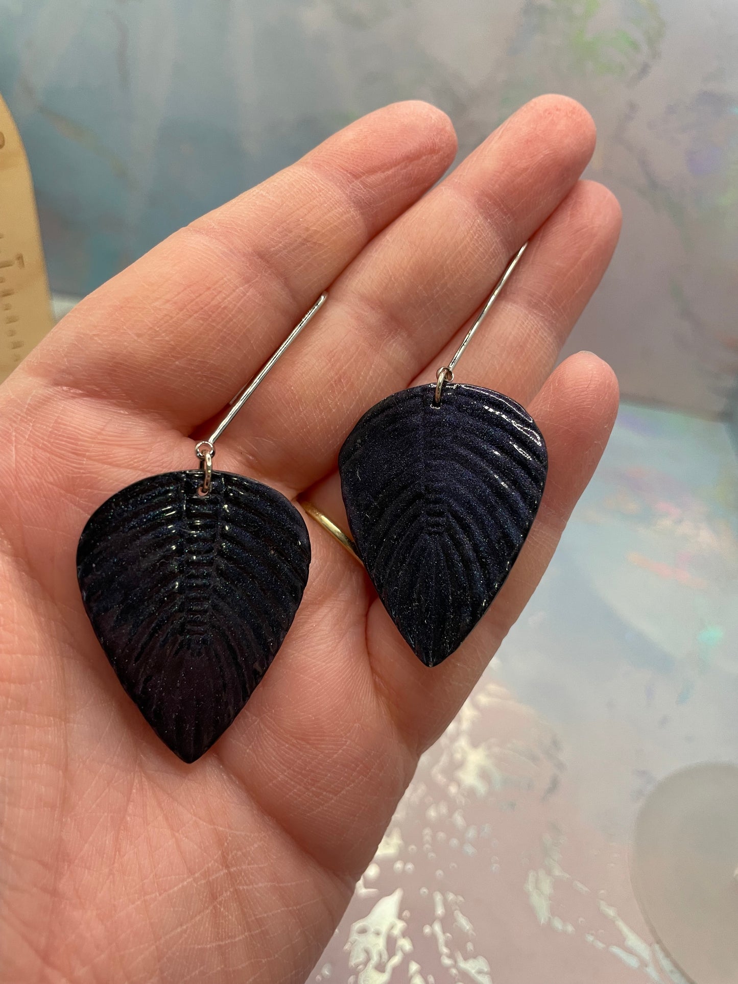 Black leaf-shaped earrings held in a hand with a blurred background