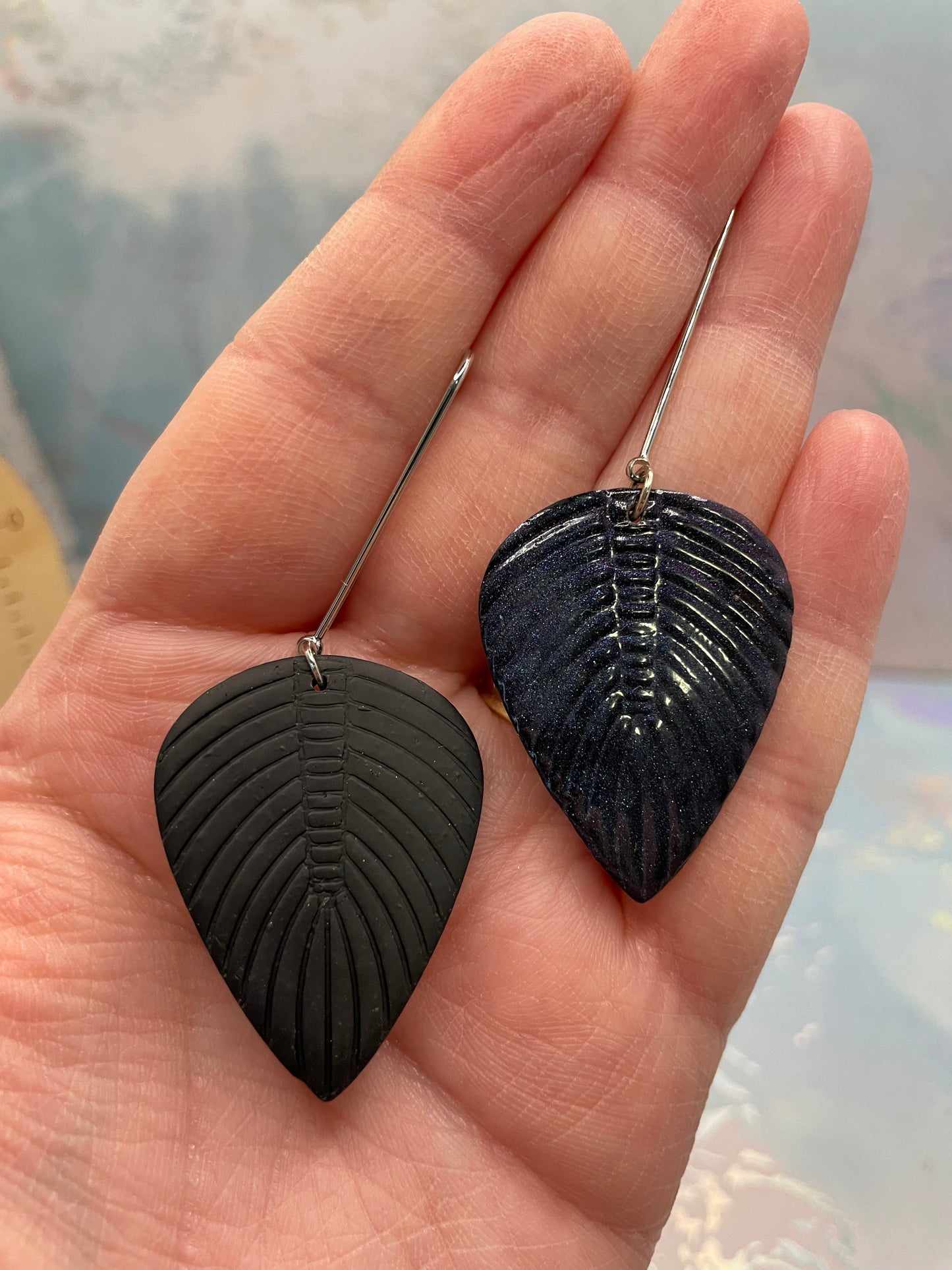 Black leaf-shaped earrings held in a hand against a neutral background