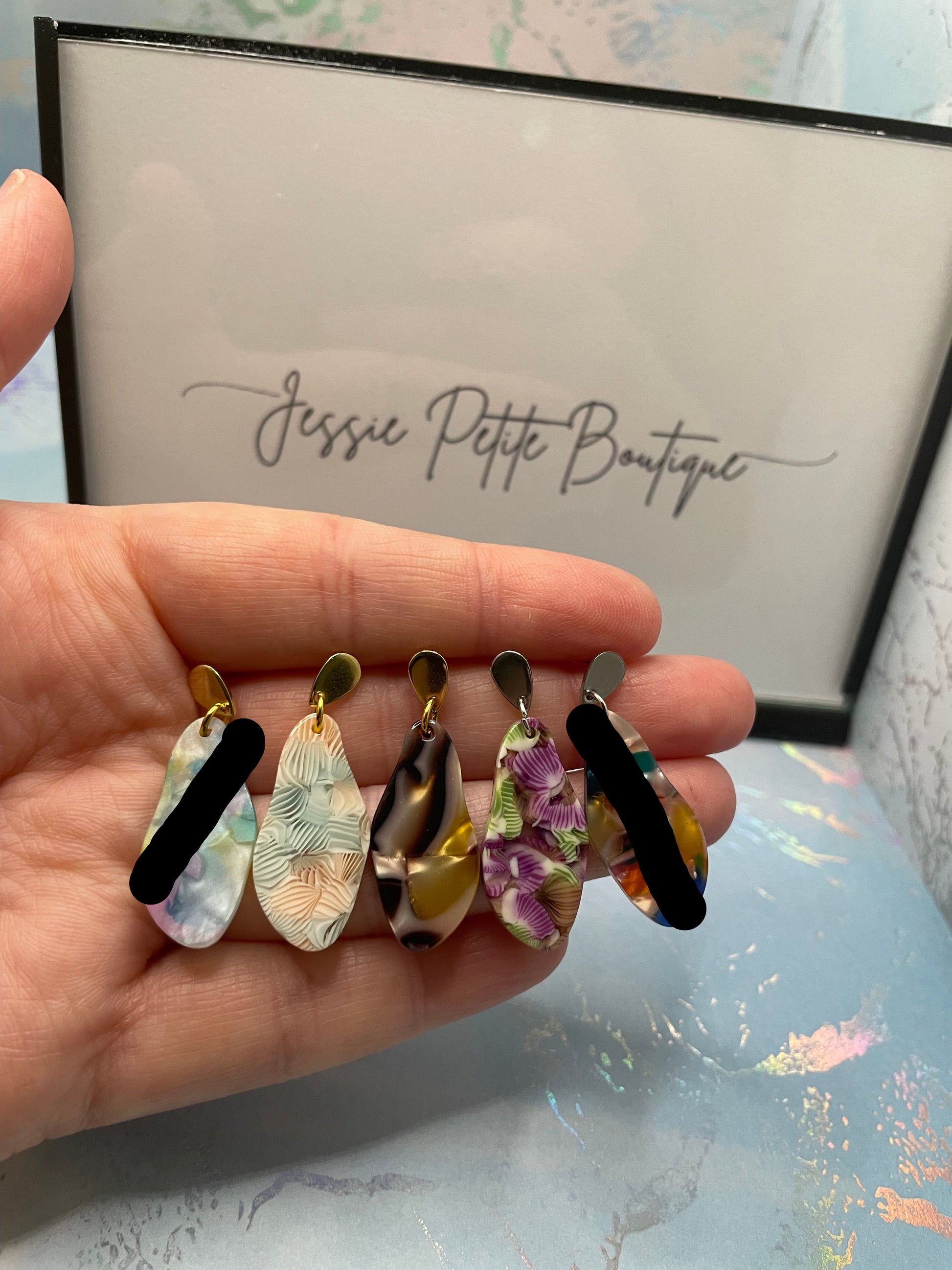 Hand holding colourful earrings with a branded box in the background