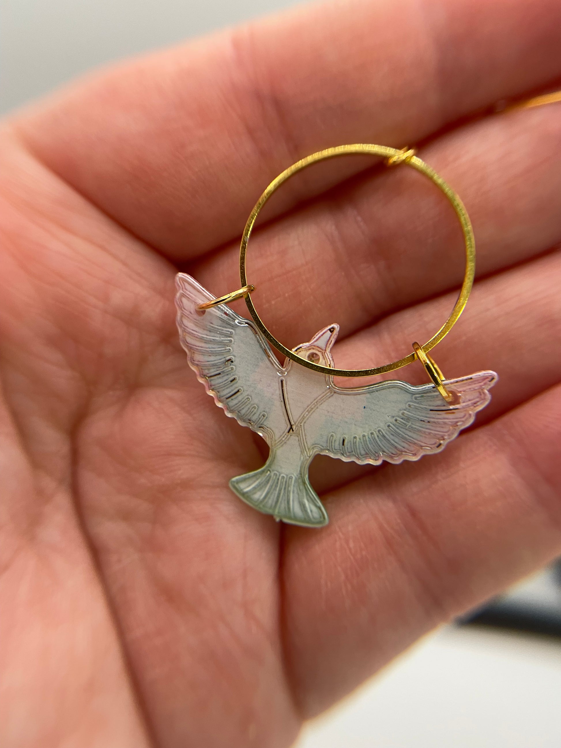 Gold hoop earring with a bird-shaped charm held in a hand.