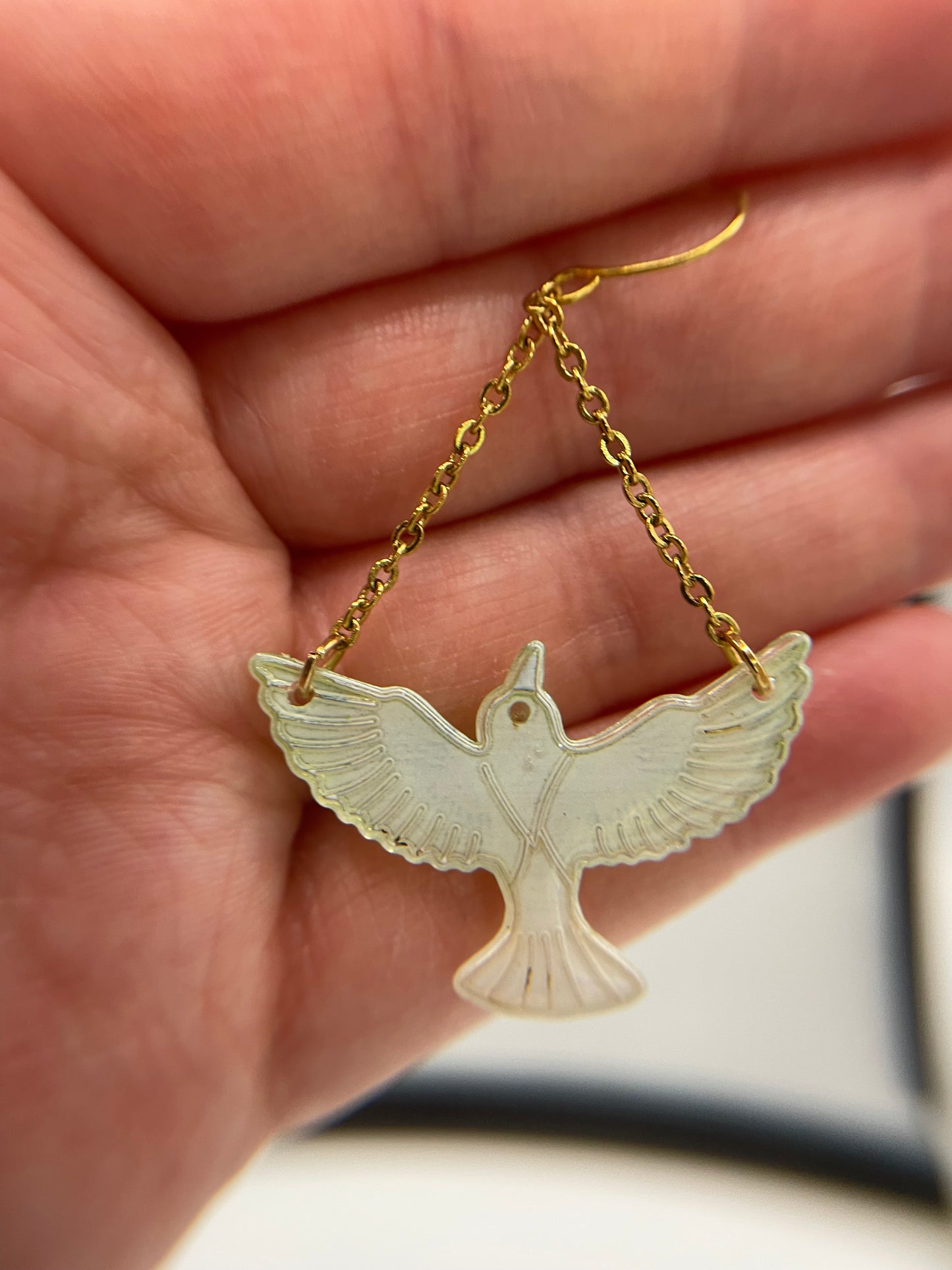 Bird-shaped pendant on a gold chain held in a hand