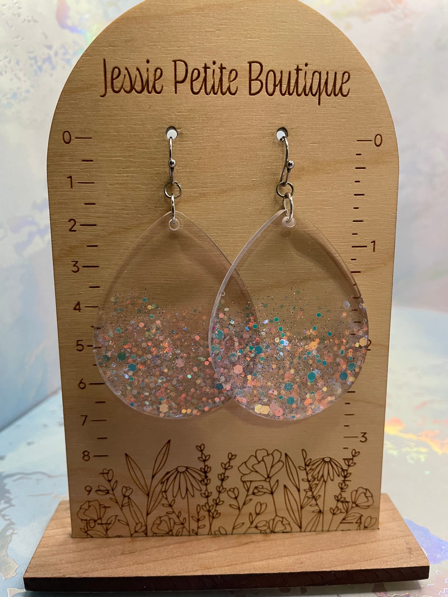 Pair of glittery earrings on a wooden display card with 'Jessie Petite Boutique' branding.