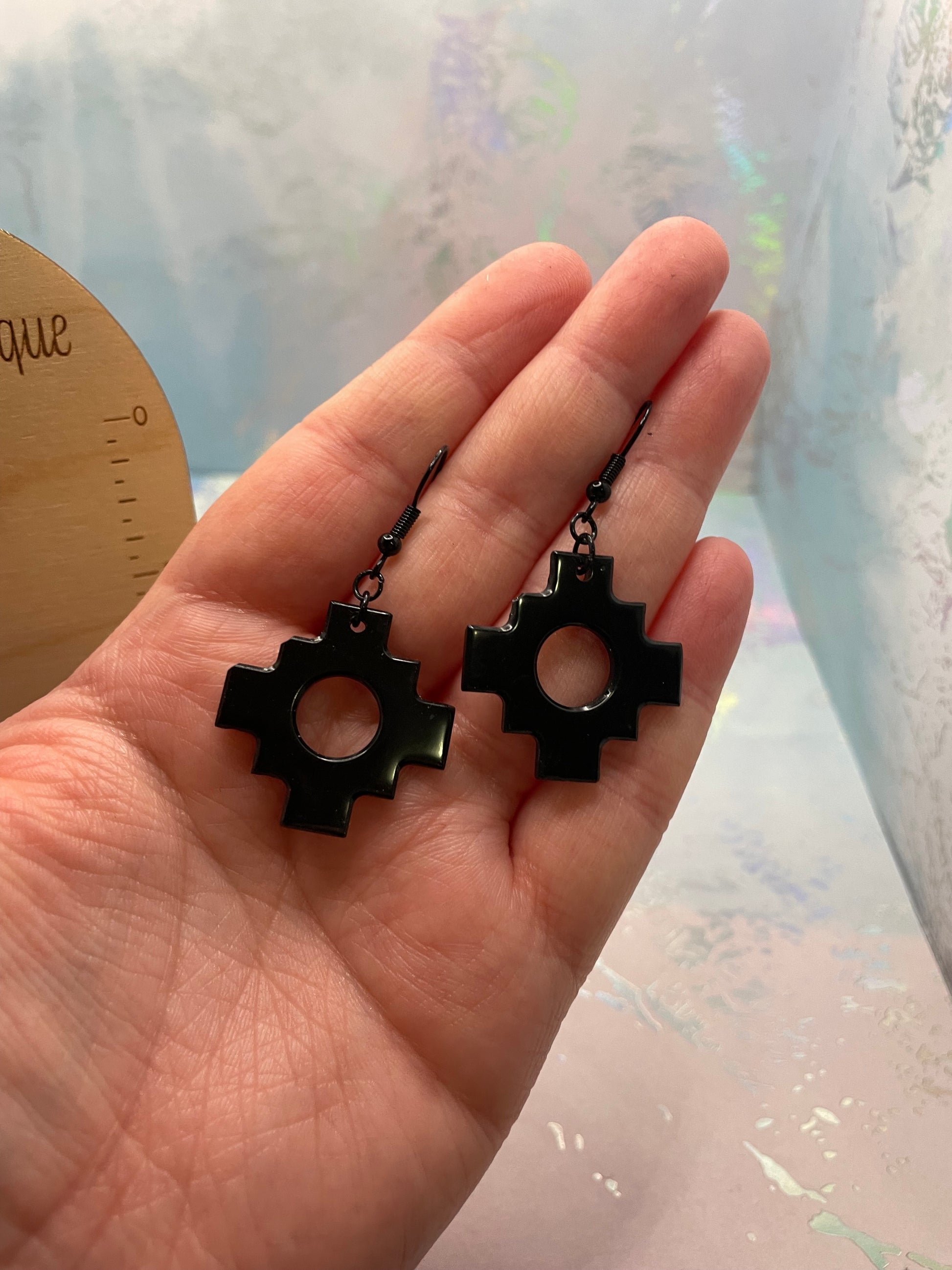 Hand holding a black geometric pendant earrings against a blurred background