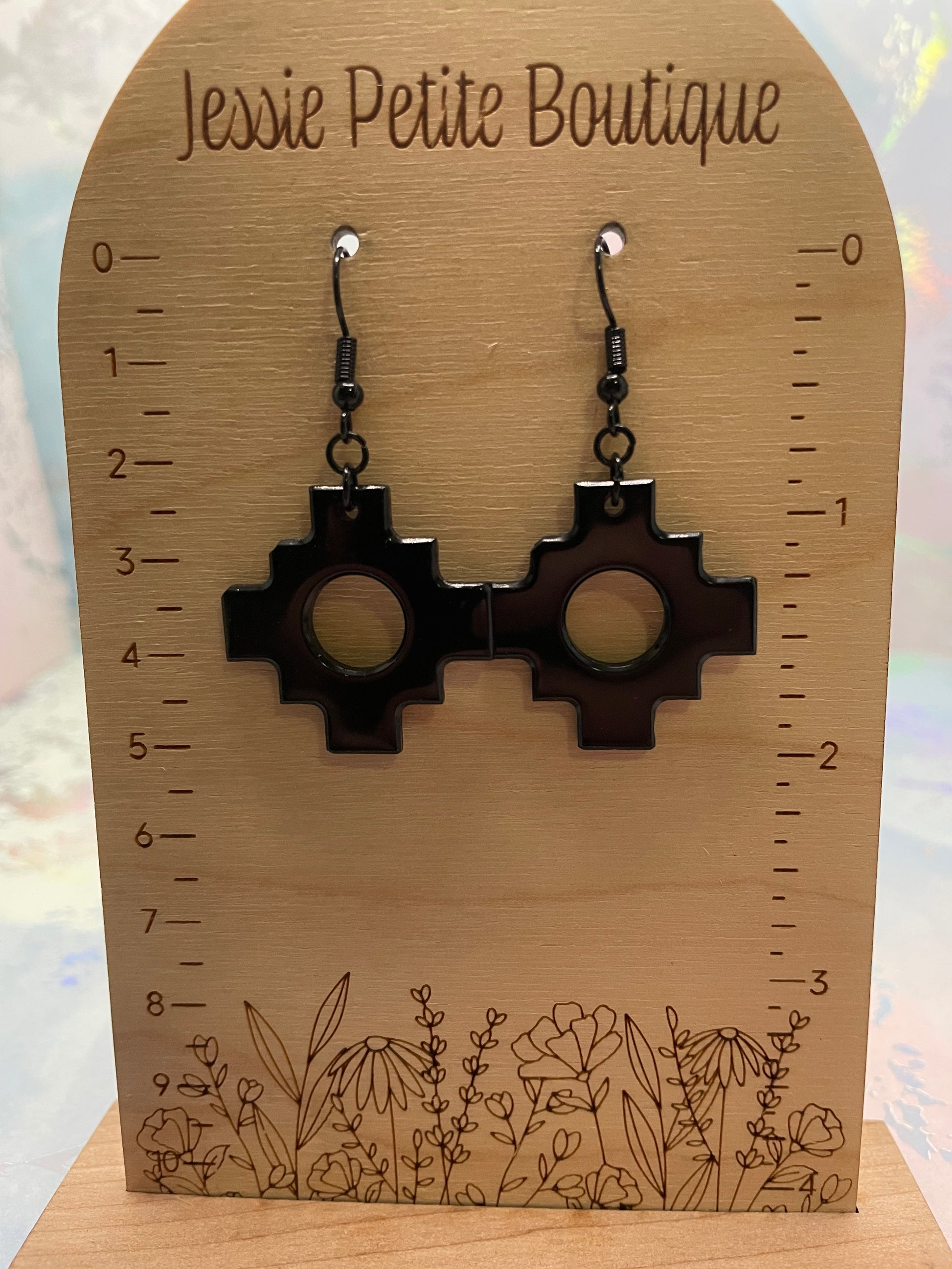 Pair of black earrings on a wooden card with floral design and measurement scale, branded 'Jessie Petite Boutique'.