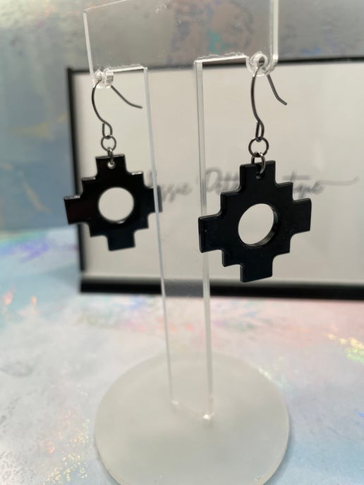 Black geometric earrings on clear stands with a blurred background