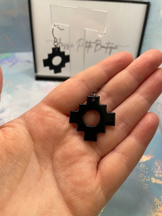 Black geometric earring held in a hand with a blurred background