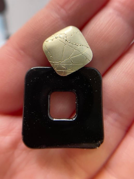 Black square object with a green stone on top held in a hand.