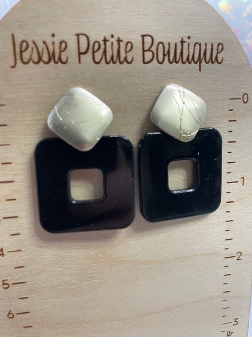 Pair of earrings with black square bases and white stone tops on a wooden surface with 'Jessie Petite Boutique' branding.