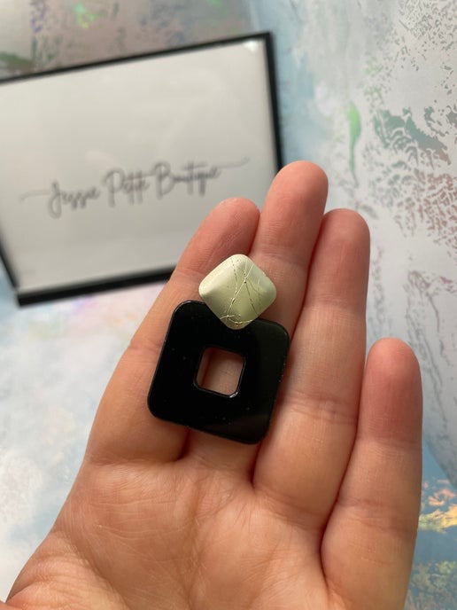 Hand holding a black square earring with a white stone, with 'Jessica Pettit Boutique' card in the background.