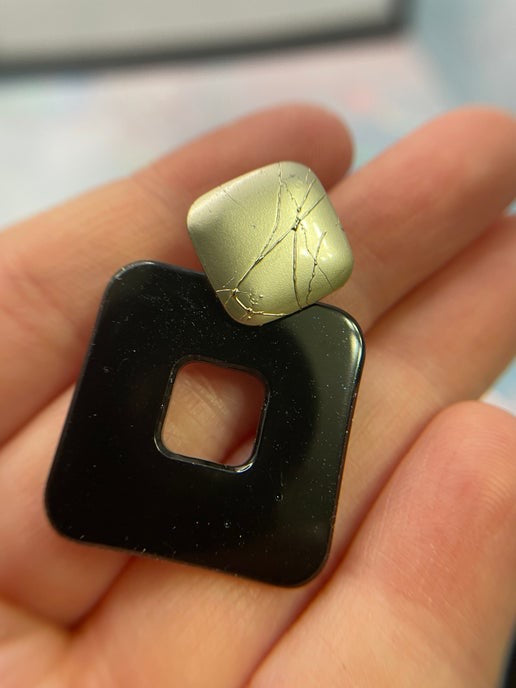 Black and gold square-shaped pendant held in a hand with a blurred background