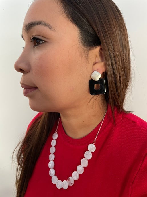 Woman wearing a white beaded necklace and black earrings on a plain background