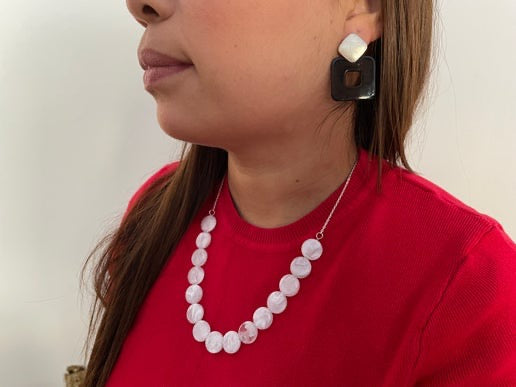 Person wearing a red top and white pearl necklace with a neutral background