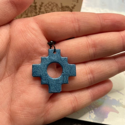 Blue cross-shaped pendant held in a hand with a blurred background