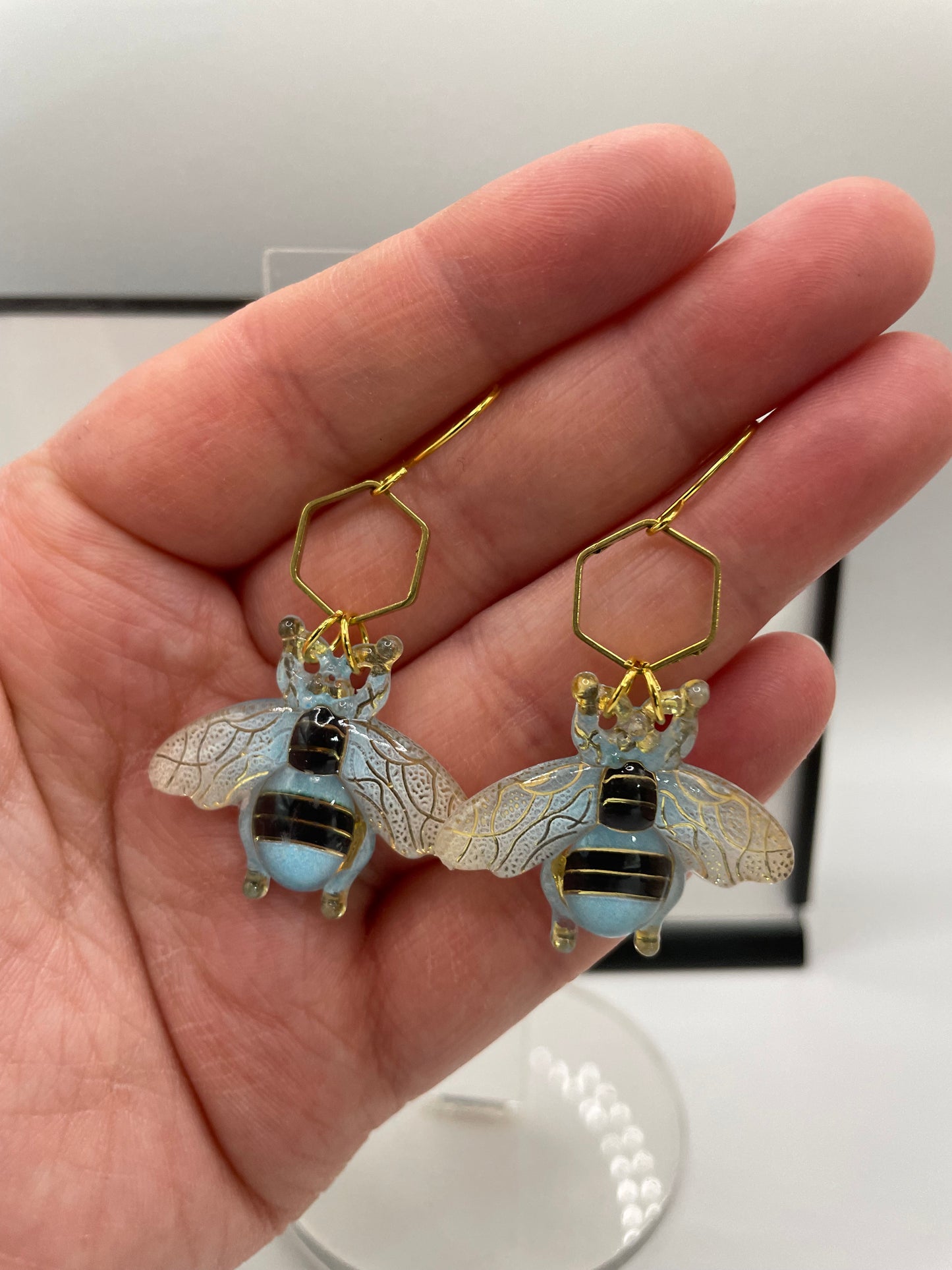 Hand holding bee-shaped earrings with gold and black details