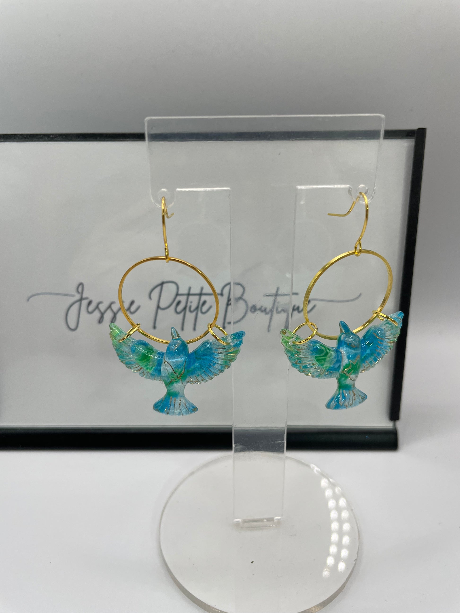 Gold hoop earrings with blue butterfly design on a clear stand against a white background