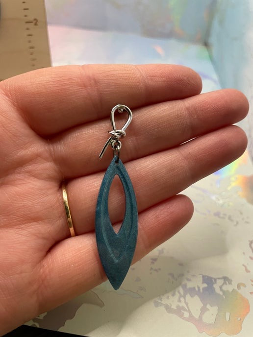 Blue teardrop-shaped earring on a hand with a blurred background
