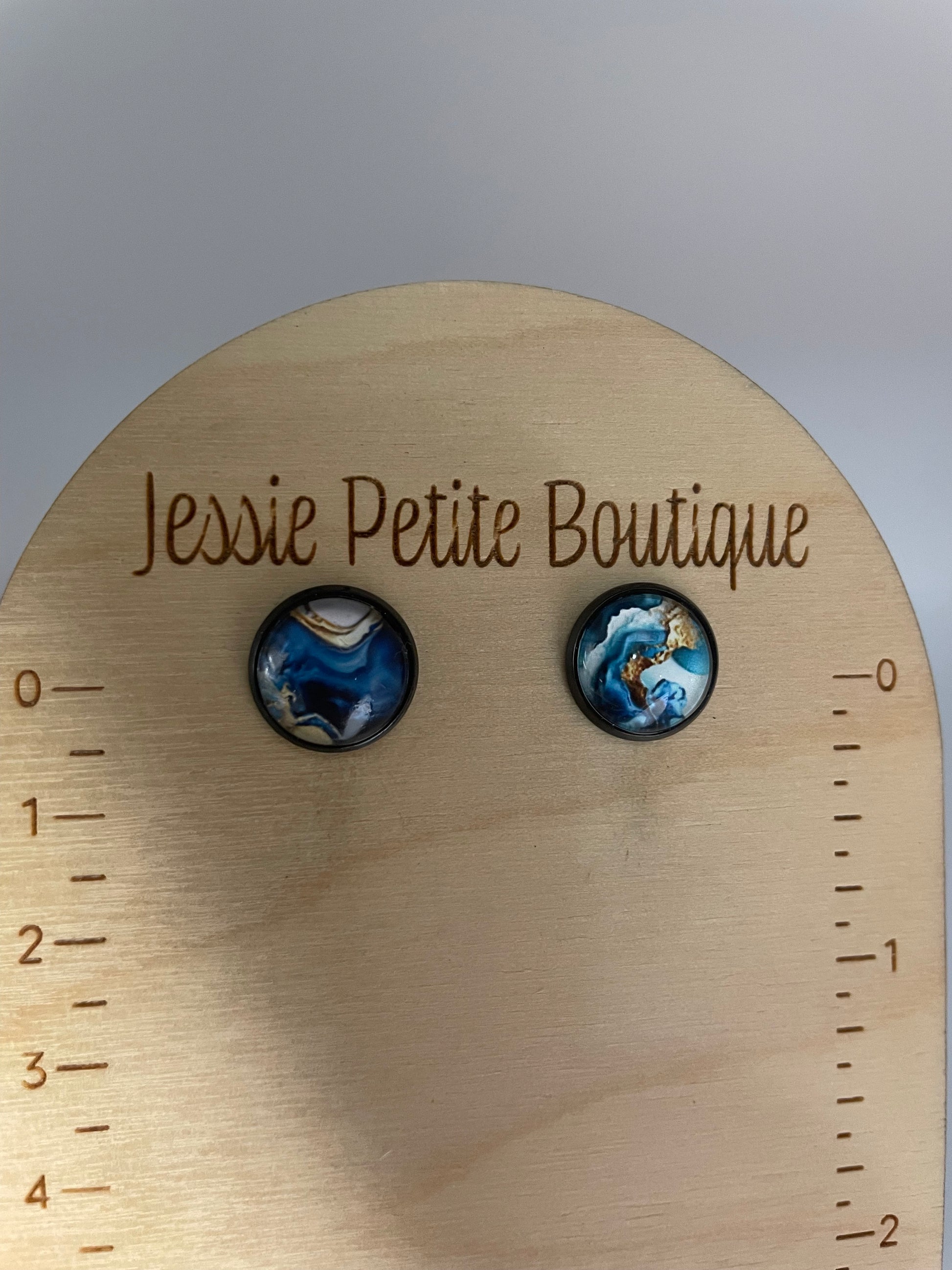 Pair of blue and black marbled earrings on a wooden round card with 'Jessie Petite Boutique' branding.
