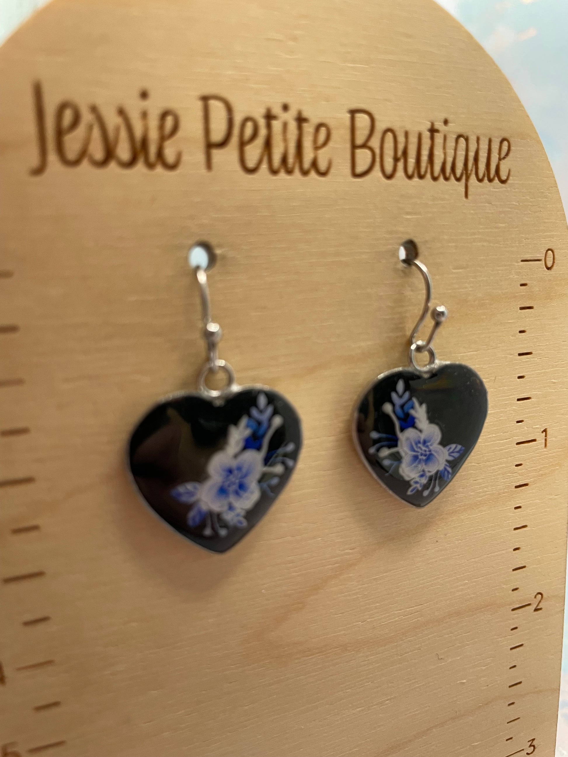 Heart-shaped earrings with floral design on a wooden board with 'Jessie Petite Boutique' branding.