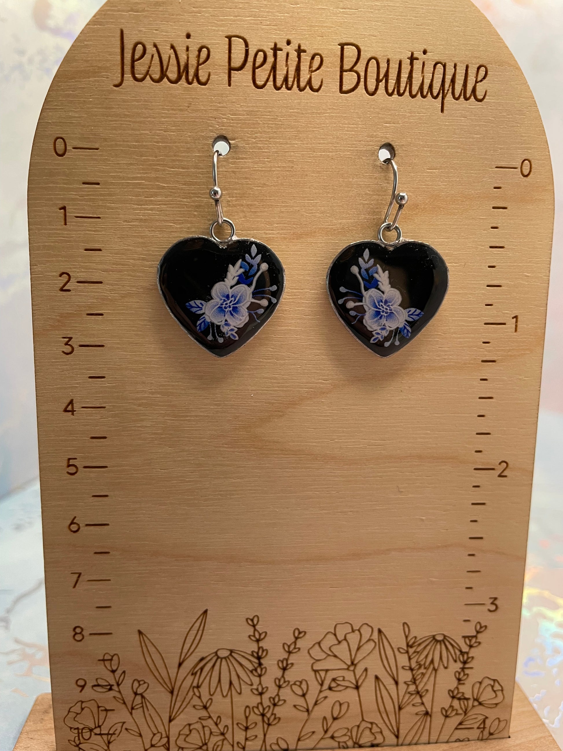 Heart-shaped earrings with floral design on a wooden ruler with 'Jessie Petite Boutique' branding.