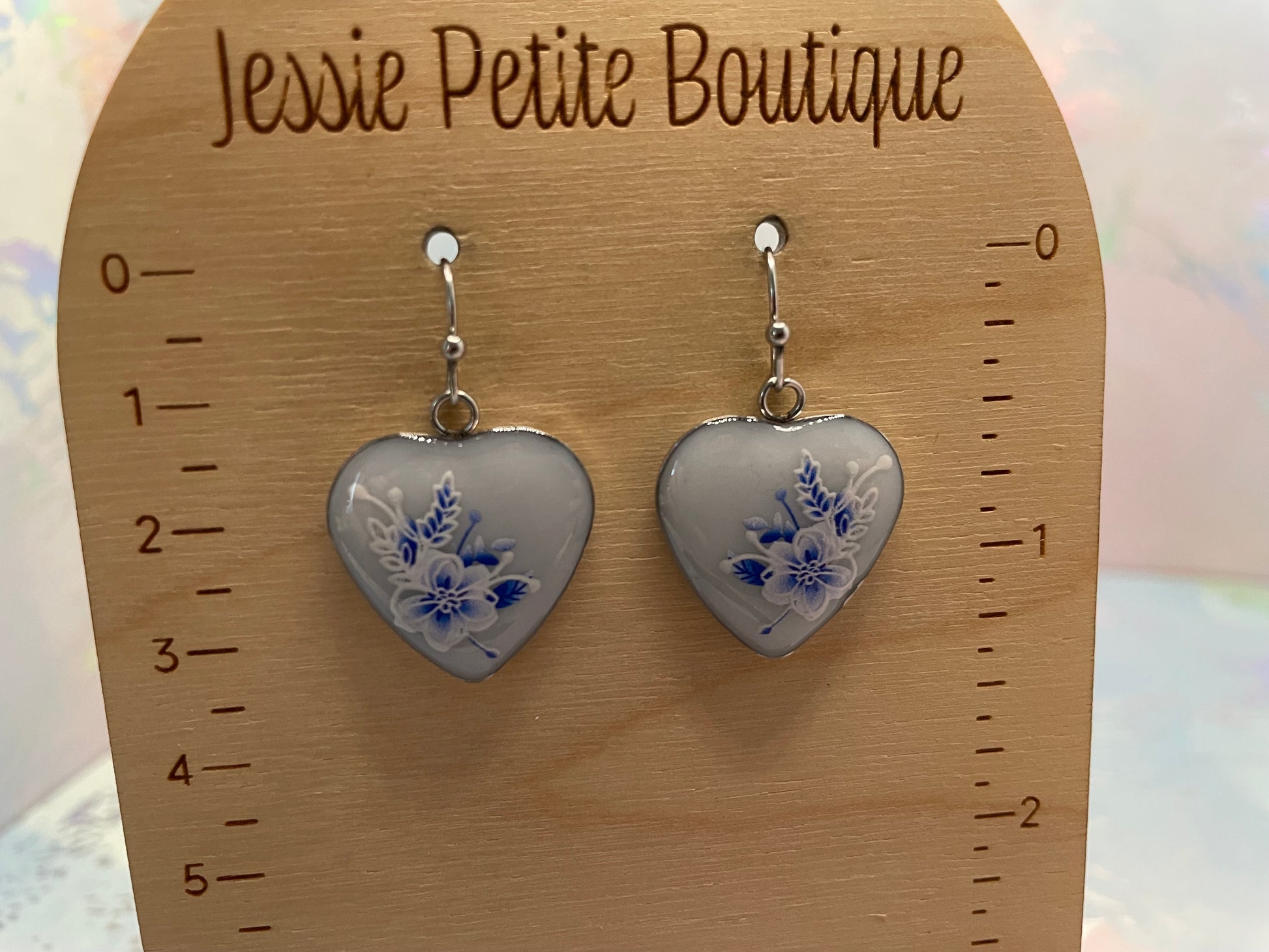Heart-shaped earrings with floral design on a wooden card with 'Jessie Petite Boutique' branding.